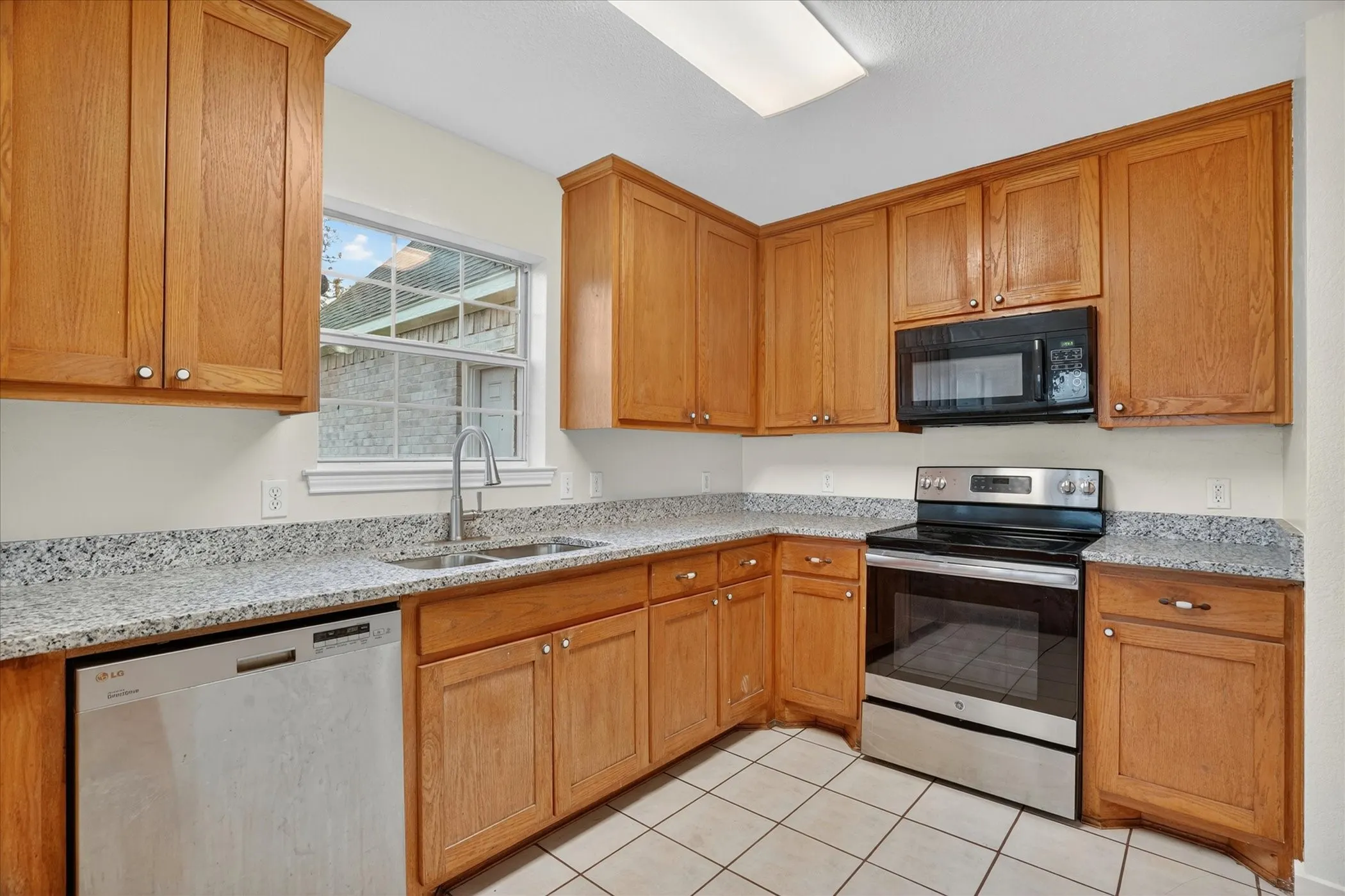 Corner kitchen with wood cabinetry, light-toned countertops, stainless steel appliances, and a window above the sink