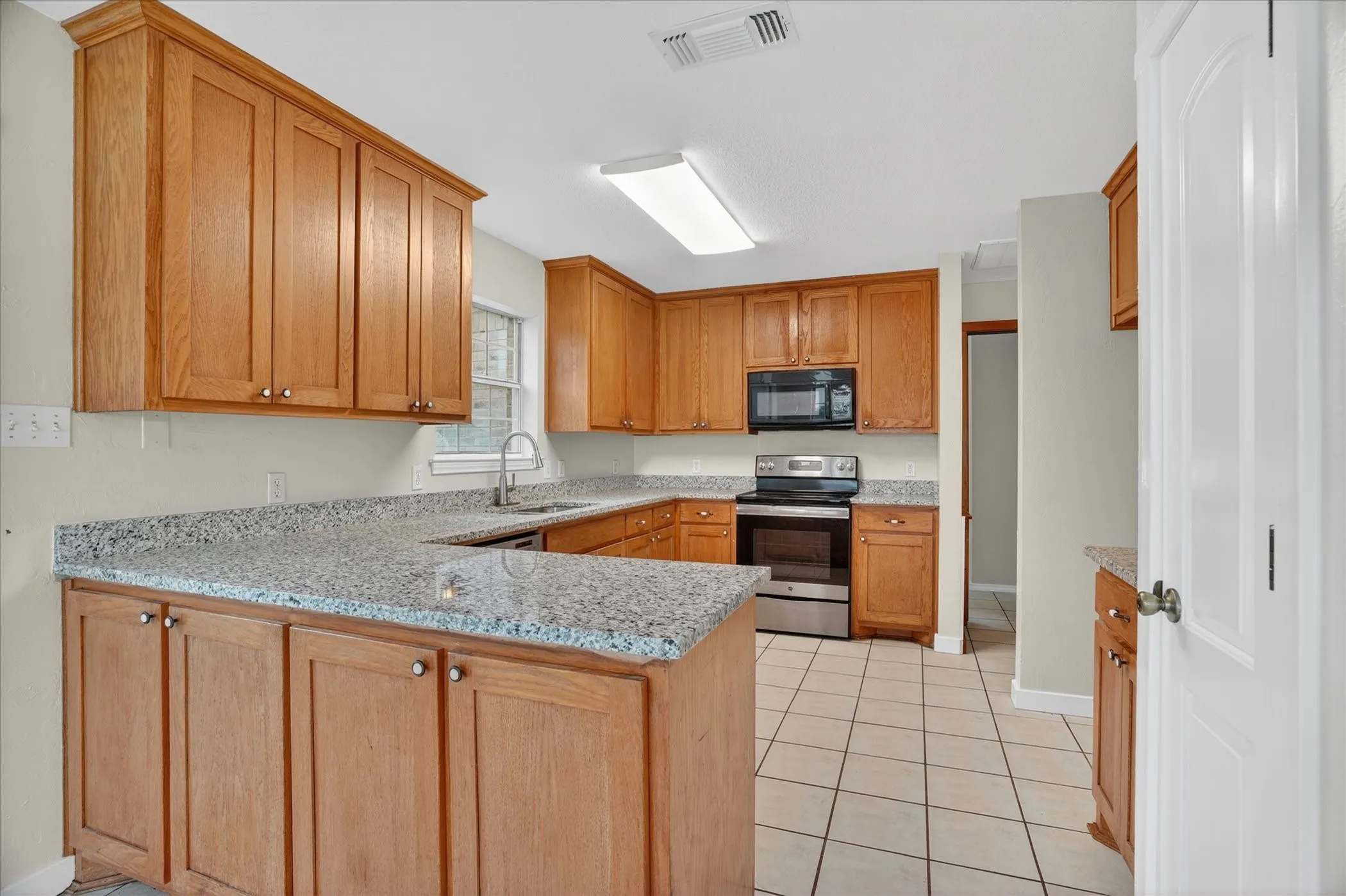 Kitchen featuring extensive wood cabinetry, light-toned countertops, stainless steel appliances, and tiled flooring