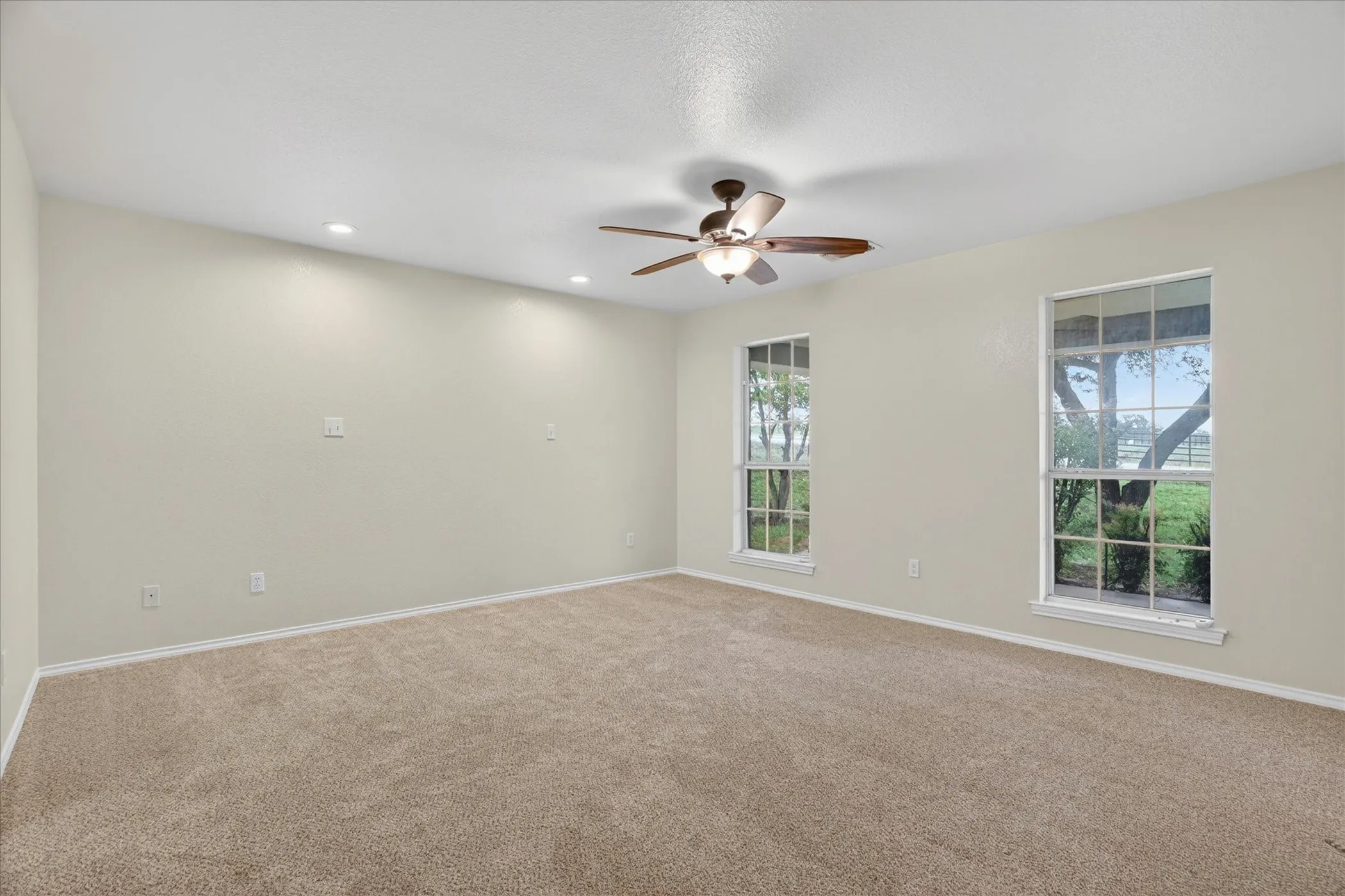 Spacious room with plush carpeting, two large windows, a ceiling fan, and recessed lighting