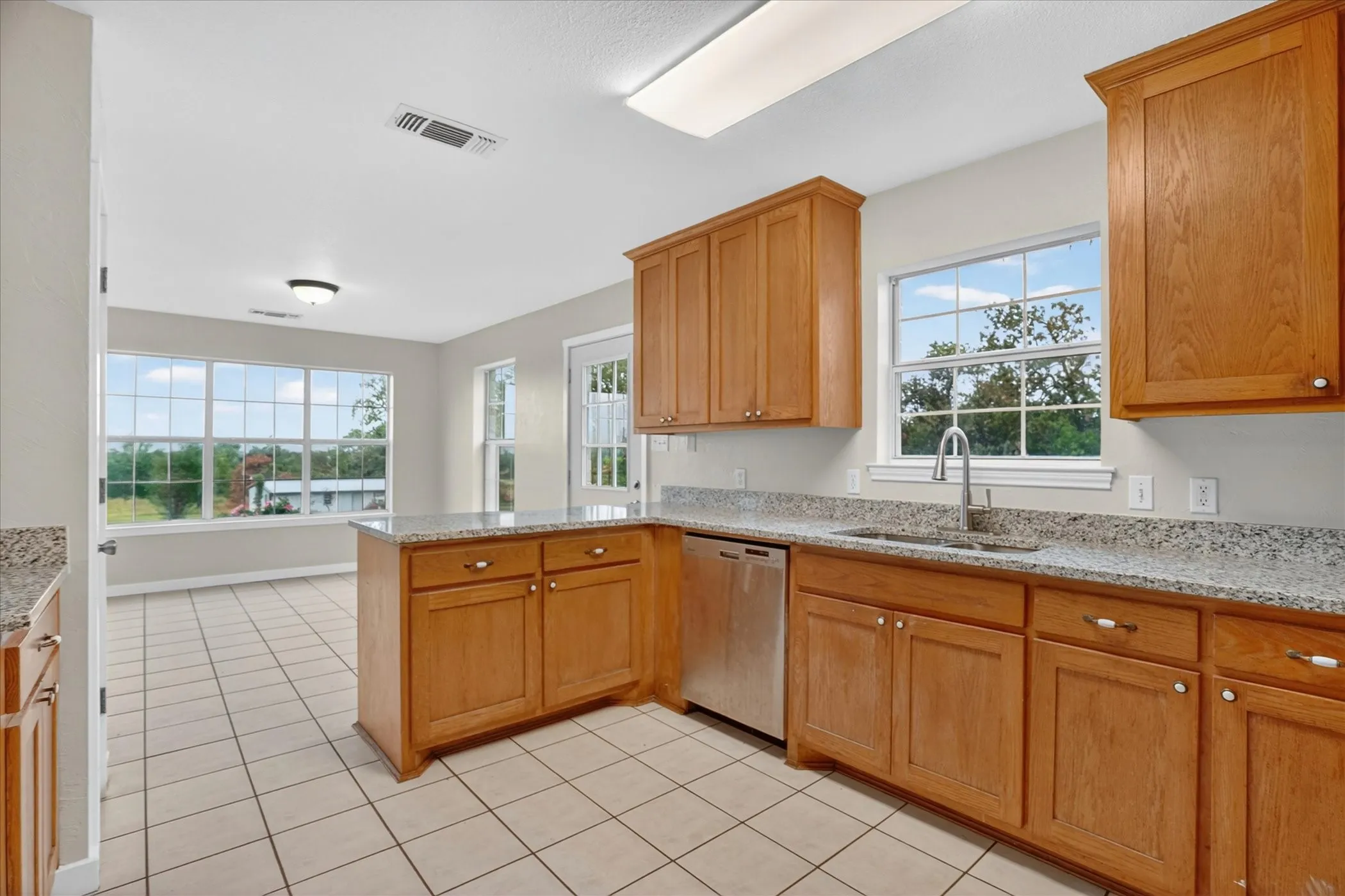 Tile flooring throughout, wood cabinetry, granite countertops, stainless steel dishwasher, and a kitchen island with storage