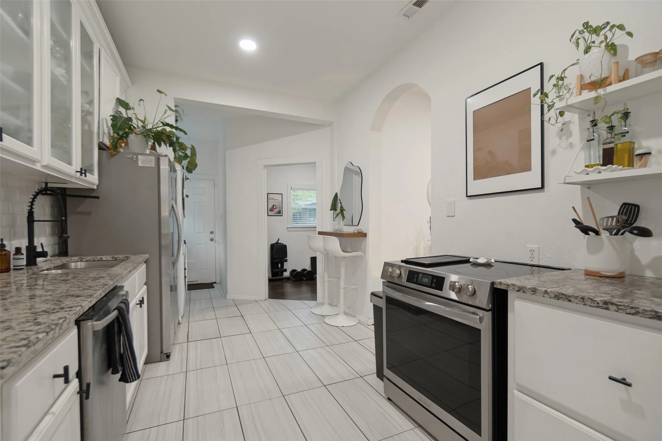 Modern kitchen featuring white cabinetry with dark hardware, stainless steel appliances, granite countertops, and tiled flooring