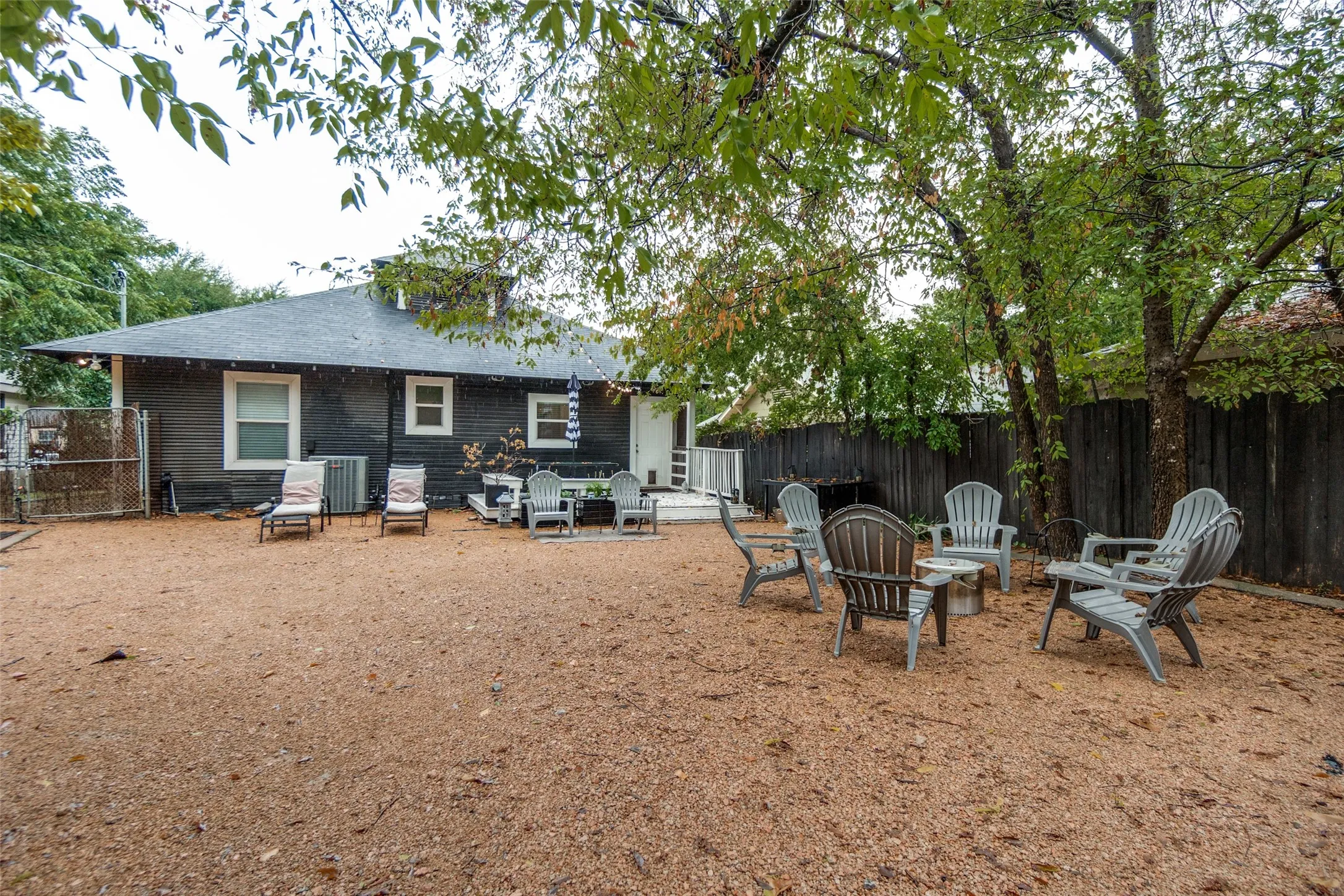 Expansive gravel yard featuring a dark wood privacy fence and mature trees