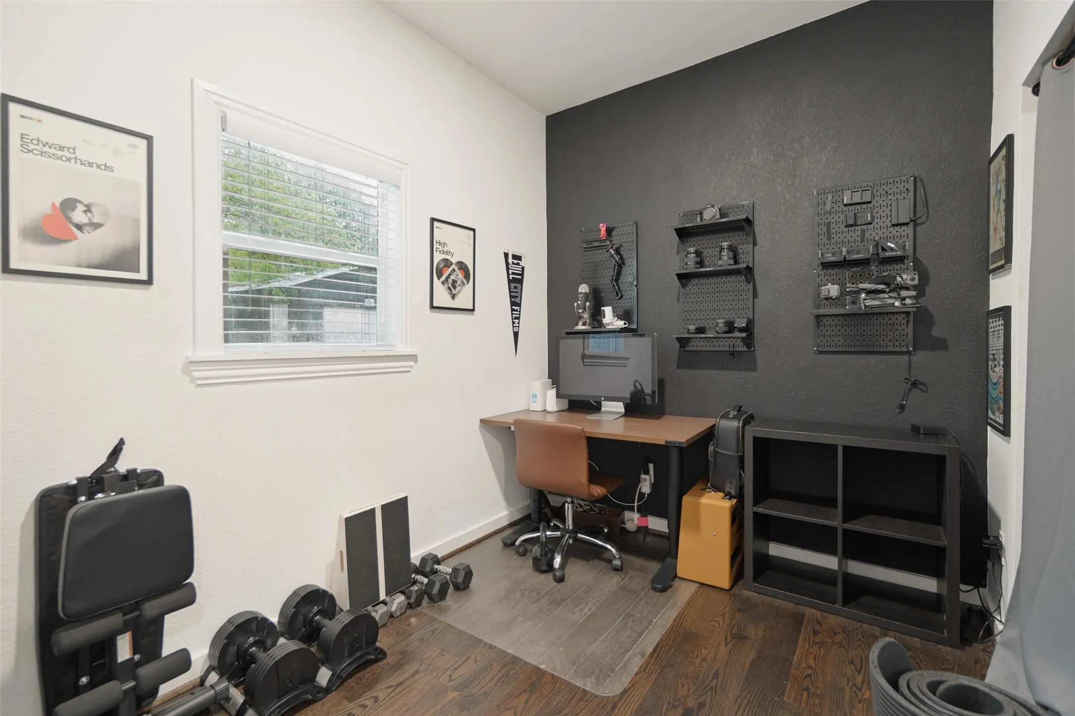 Hardwood-finish flooring, a window with horizontal blinds, a dark accent wall, and a built-in desk