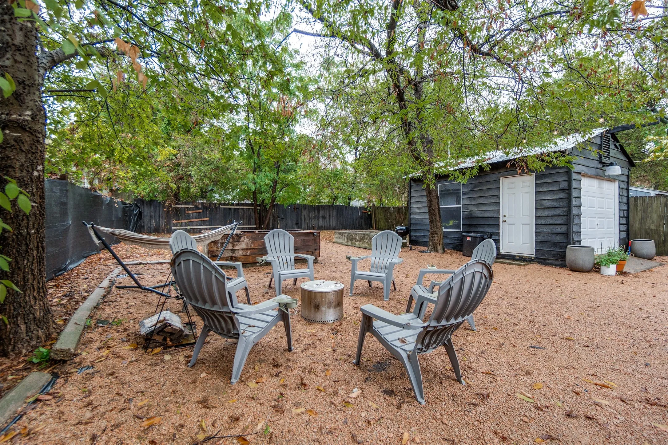 Expansive backyard featuring mature trees, a gravel ground surface, a privacy fence, and a detached structure with a white garage door and an entry door