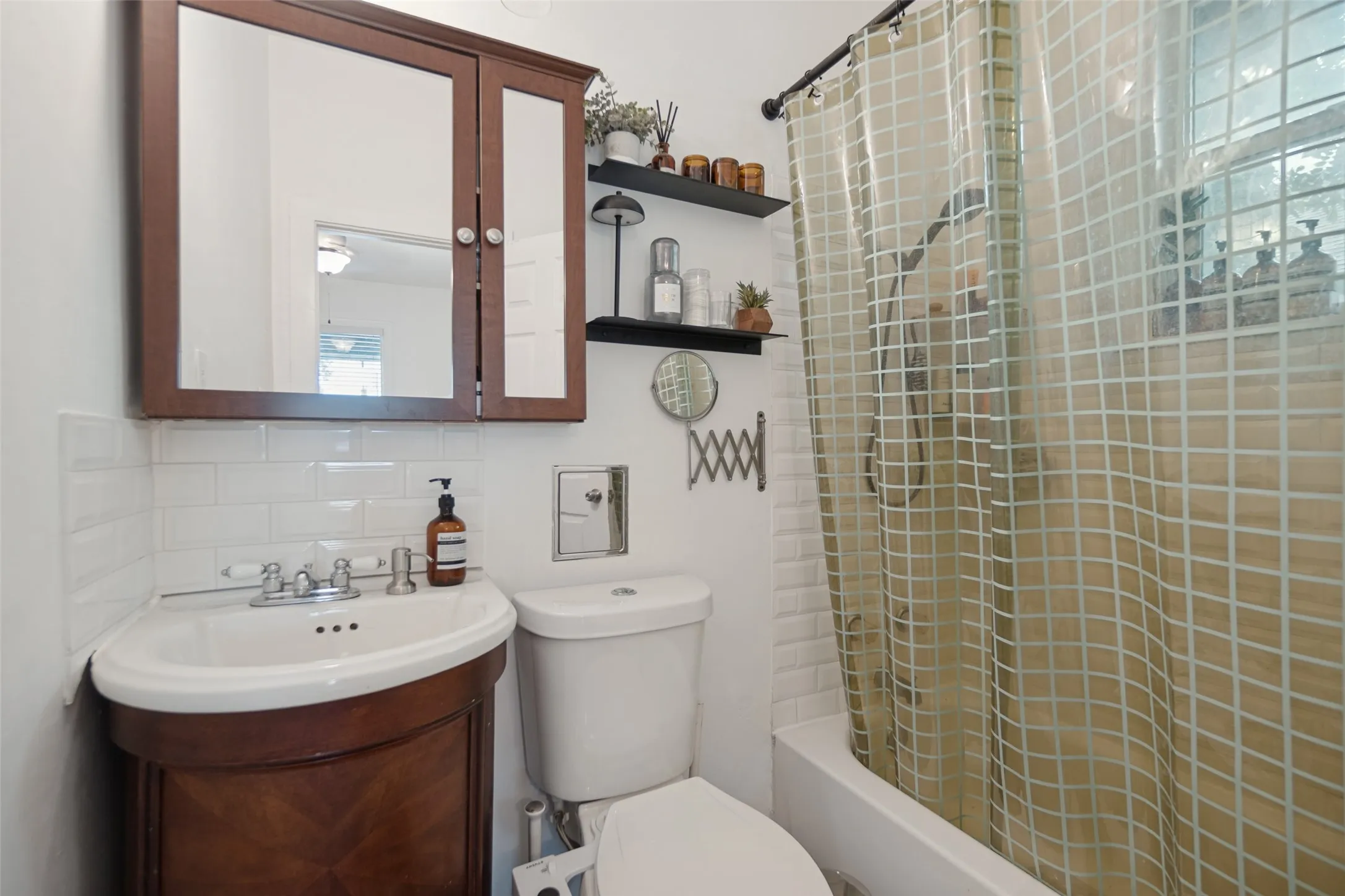 Built-in wood-finish medicine cabinet, corner vanity with undermount sink, classic subway tile backsplash, and full shower/tub combination