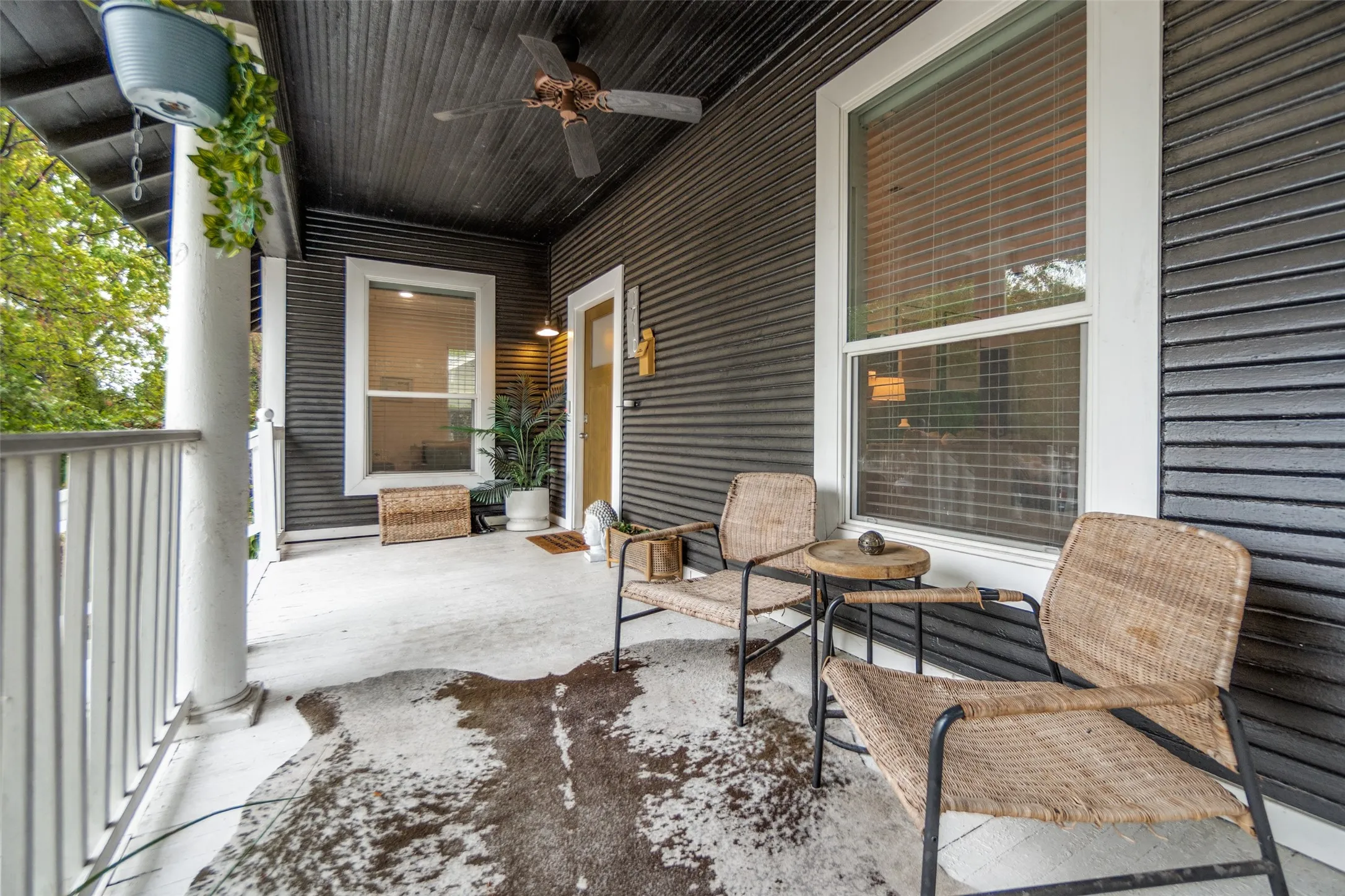 Covered front porch featuring a dark paneled ceiling, white support columns, and a ceiling fan