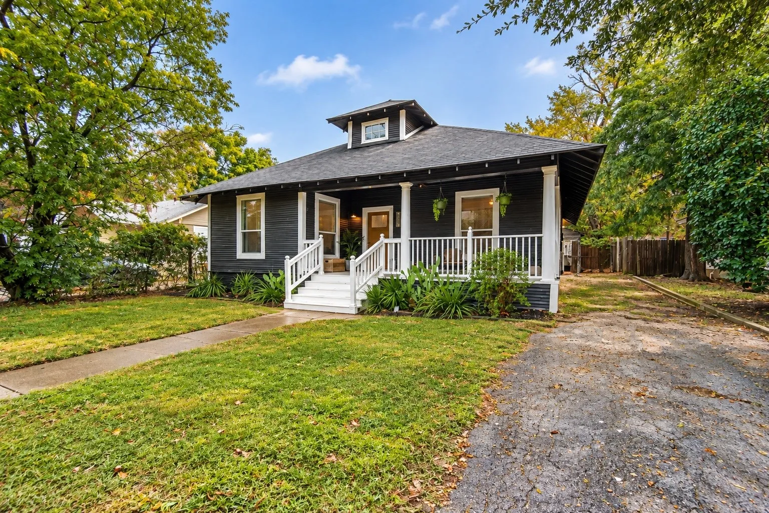 Dark siding exterior with white trim, covered porch, white porch railing, front yard, and paved driveway