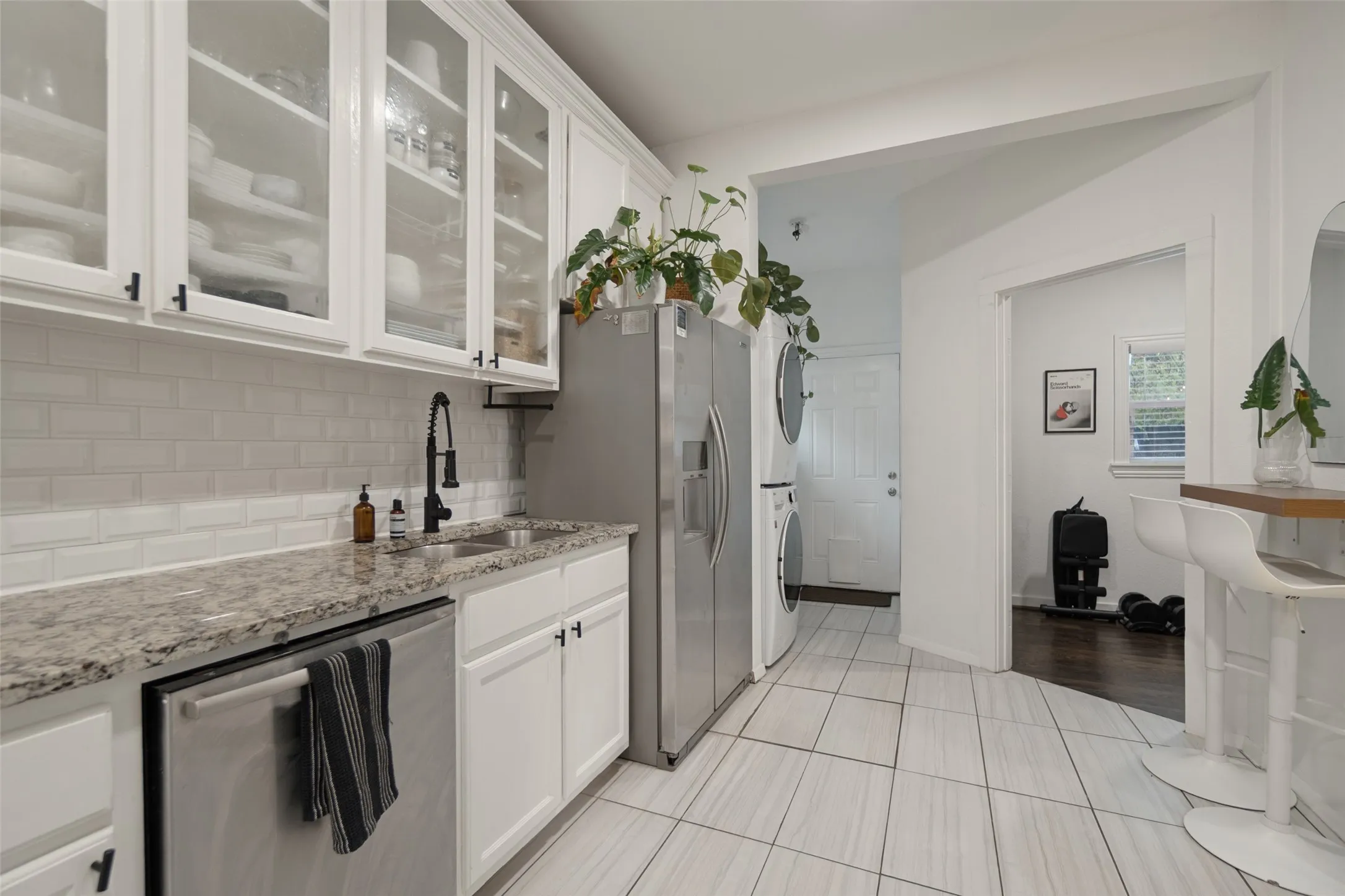 White shaker cabinetry with glass-front uppers, granite-look countertops, white subway tile backsplash, stainless steel appliances, and large format floor tile