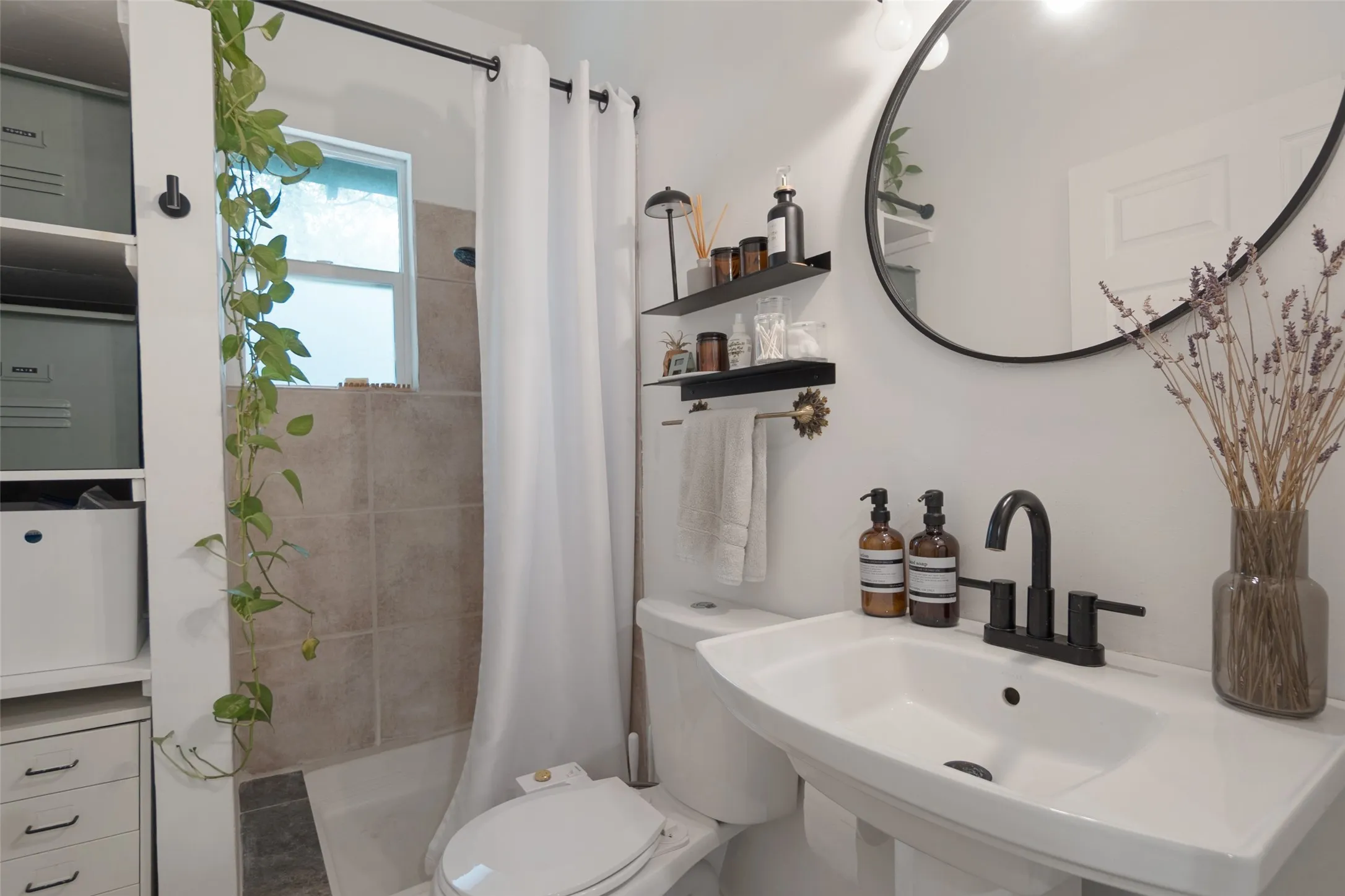 Pedestal sink with black-finish faucet, circular wall mirror, and built-in shelving