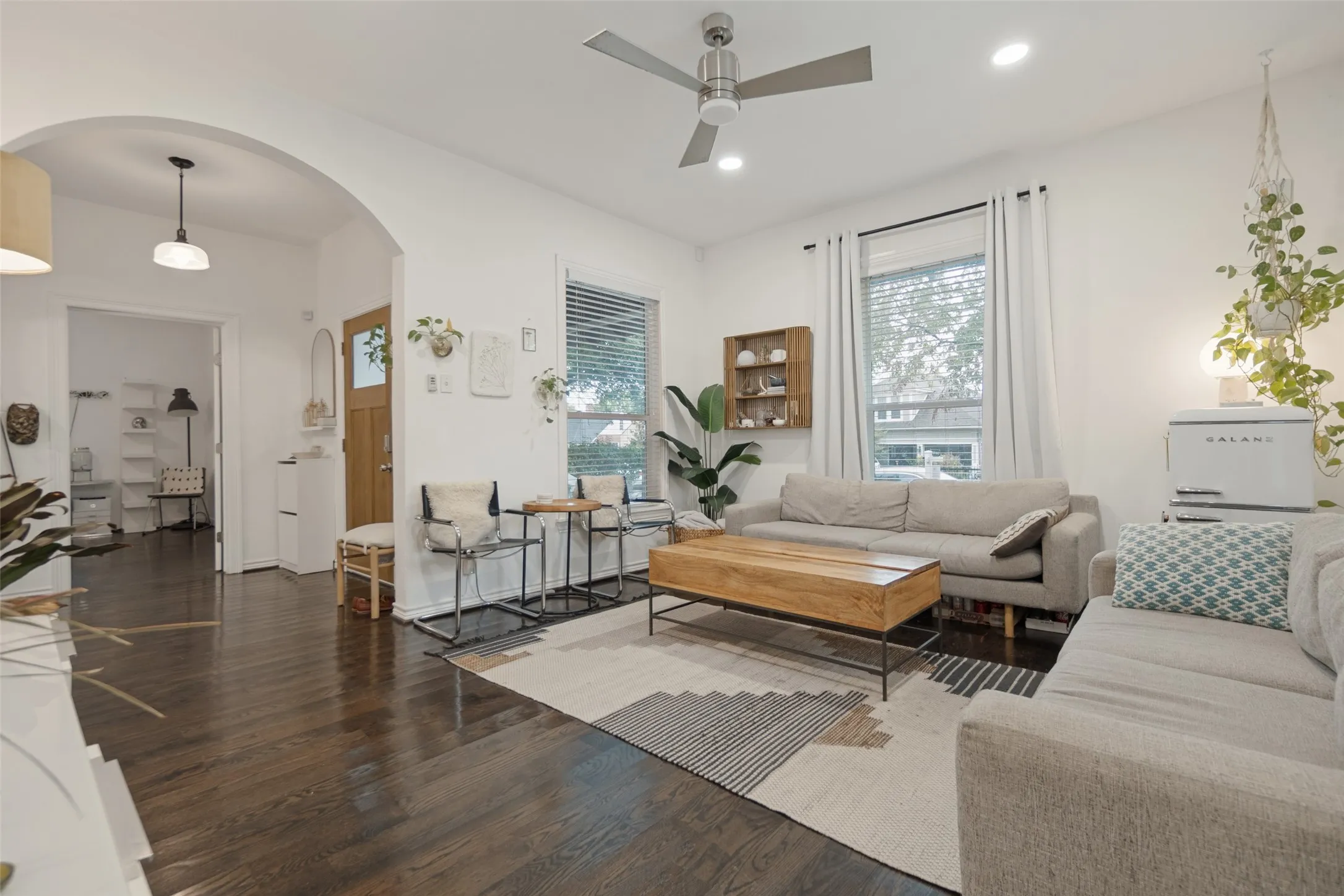 Archway entry to a bright living space featuring dark wood-finish flooring, white walls, and a ceiling fan with integrated lighting