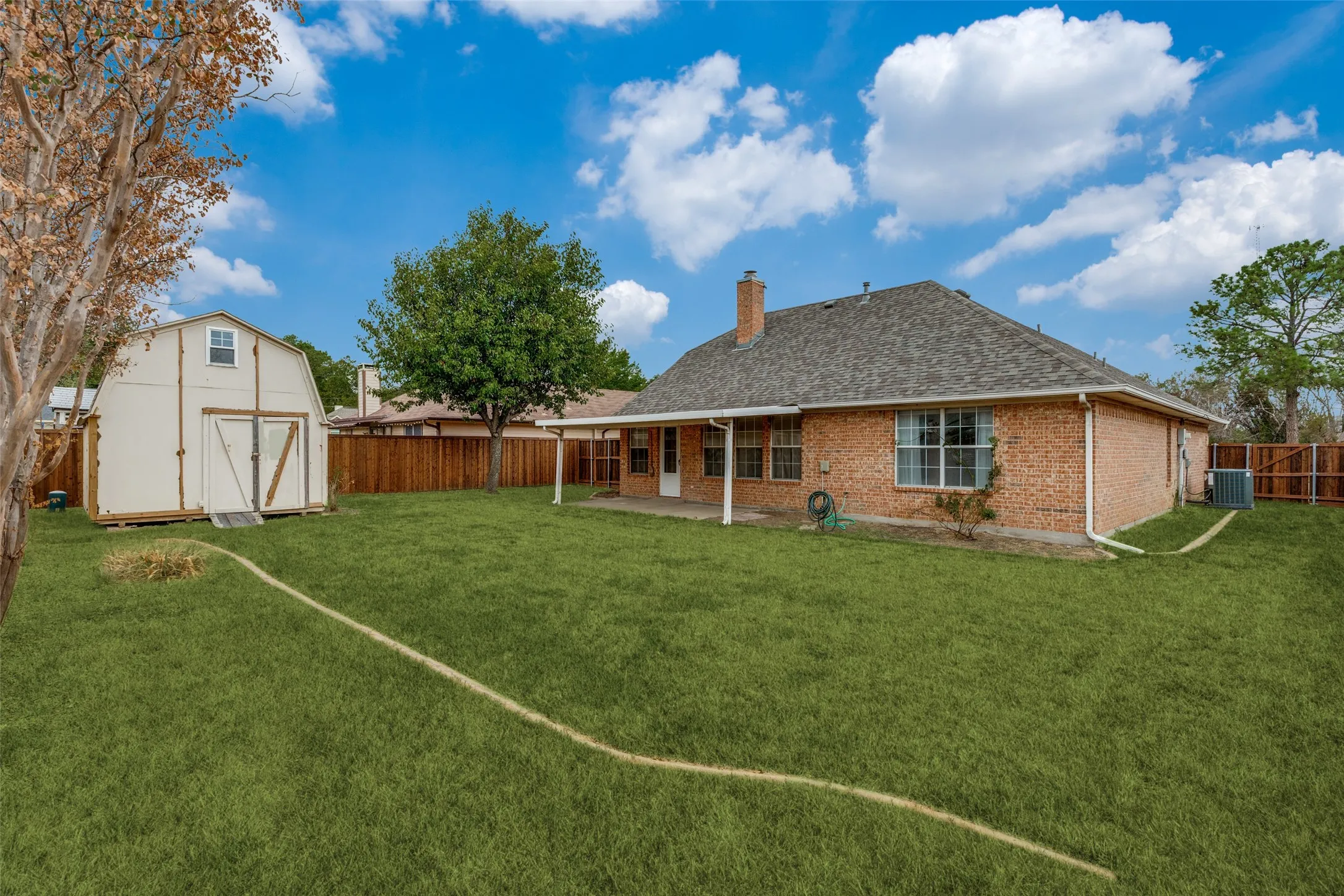 Expansive lawn featuring a brick exterior, covered patio, privacy fencing, and a detached storage shed