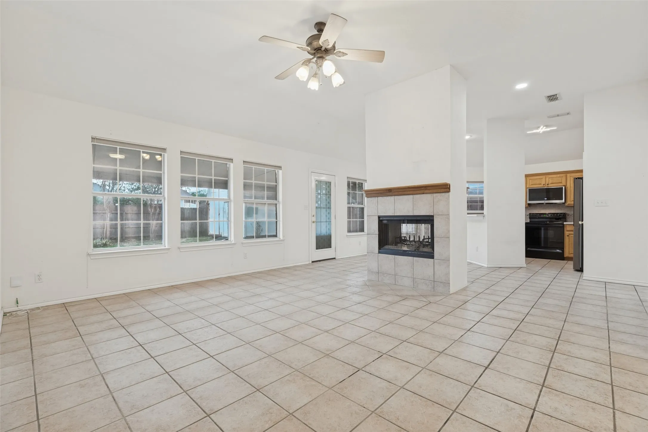 Spacious living area featuring tile flooring, multiple windows, a ceiling fan, and a fireplace with a wood mantle