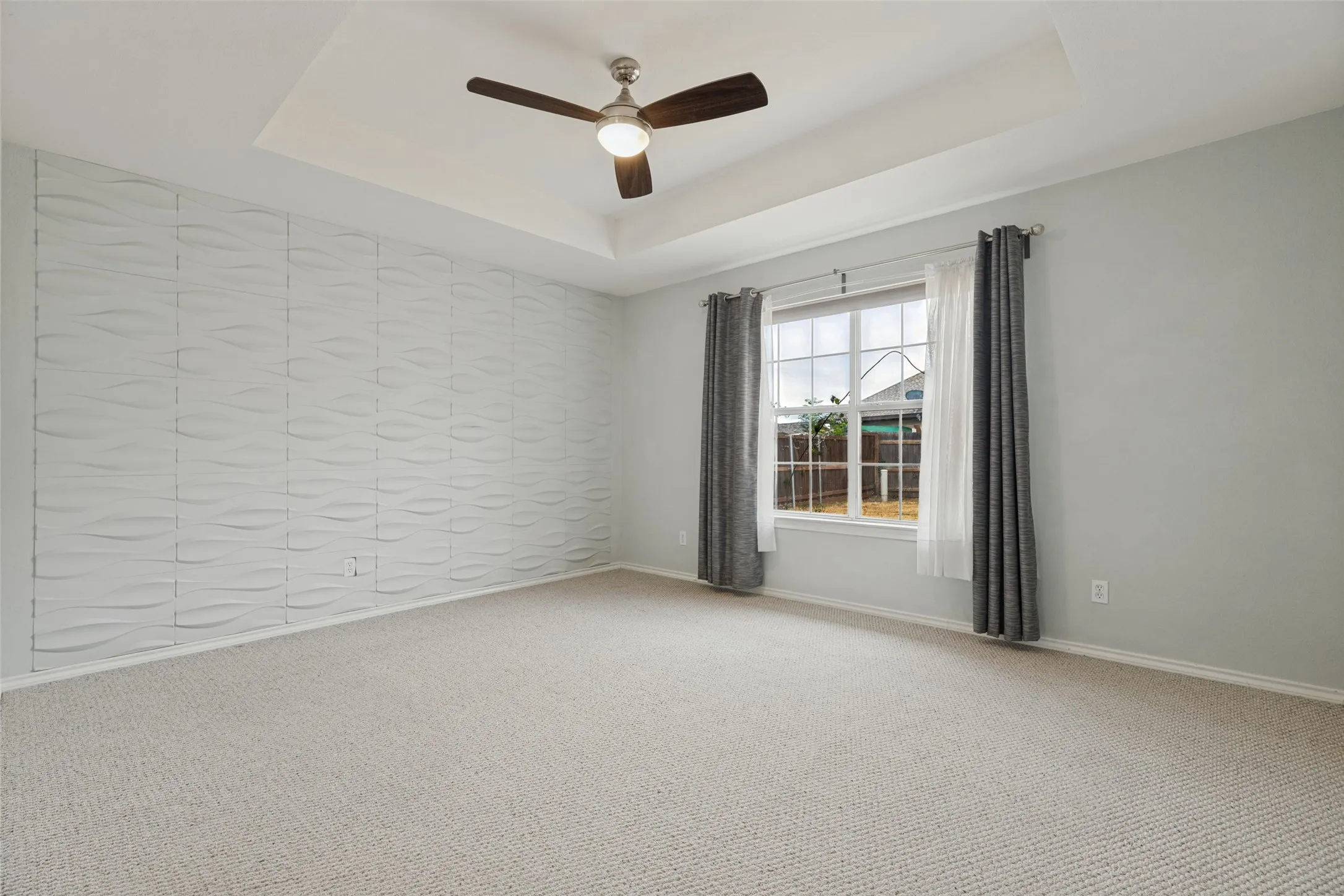 Tray ceiling with recessed lighting, textured accent wall, ceiling fan with light fixture, window with exterior exposure, and neutral carpeting