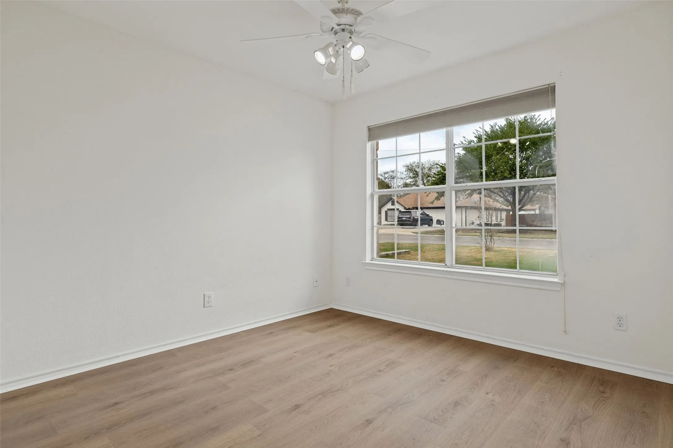 Wood-finish flooring, white walls, and a window with a roller shade