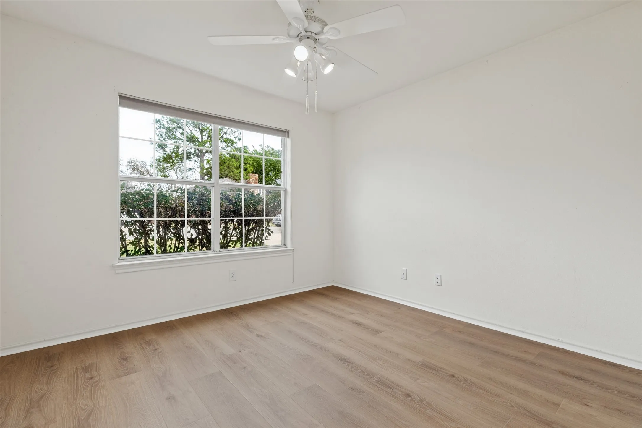 Wood-finish flooring, white walls, ceiling fan with integrated lighting, and a large window with white muntins