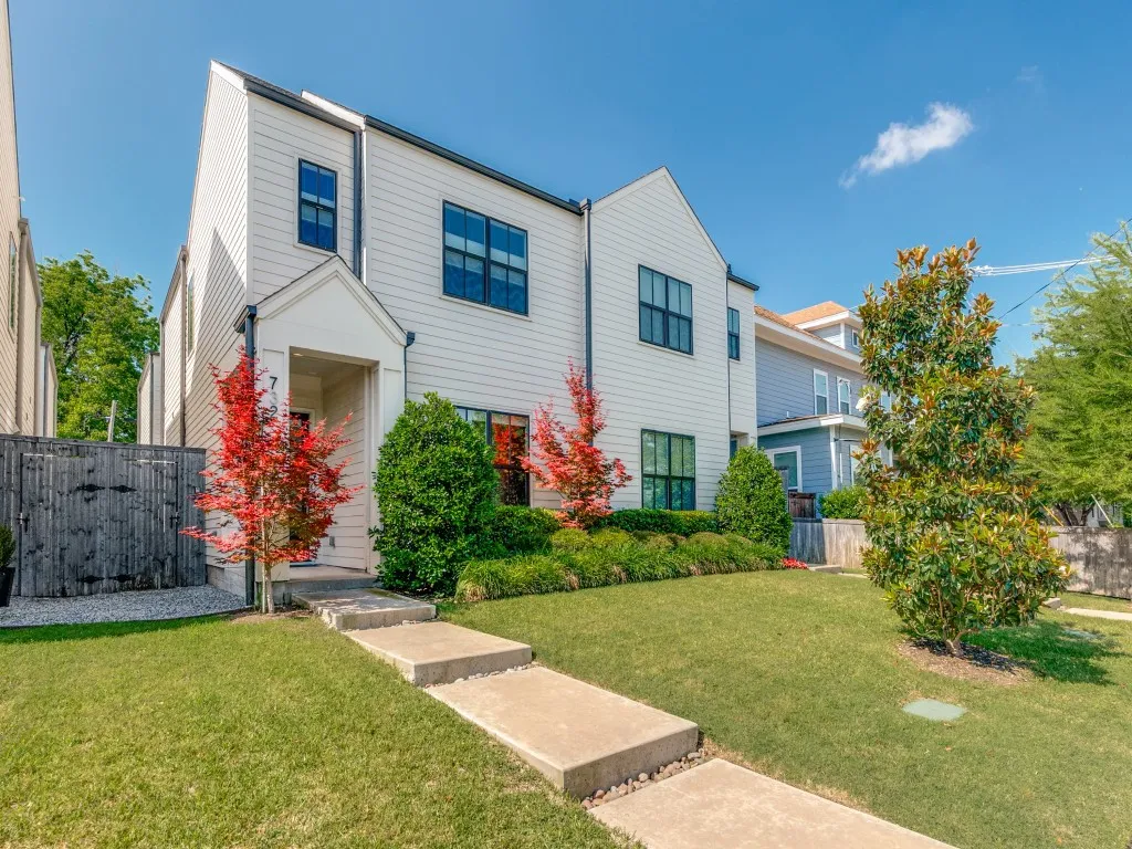 Contemporary white siding exterior featuring a covered entry, dark-framed windows, a meticulously maintained lawn, and mature landscaping