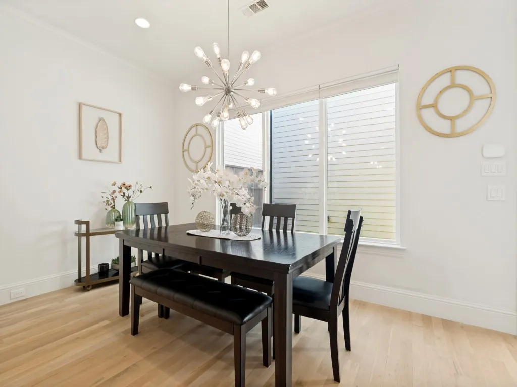 Dining area featuring a contemporary chandelier, light wood-finish flooring, and a large window with privacy blinds