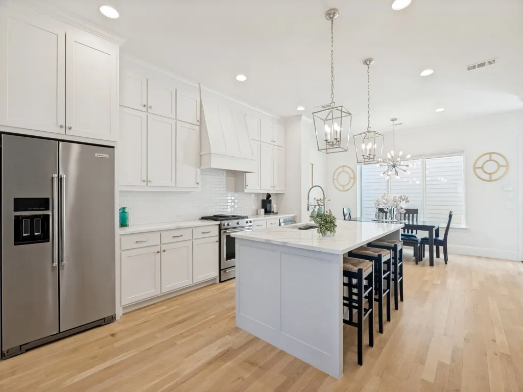 Gourmet kitchen featuring white shaker cabinetry, stainless steel appliances, a large center island with seating, pendant lighting, and light wood-finish flooring