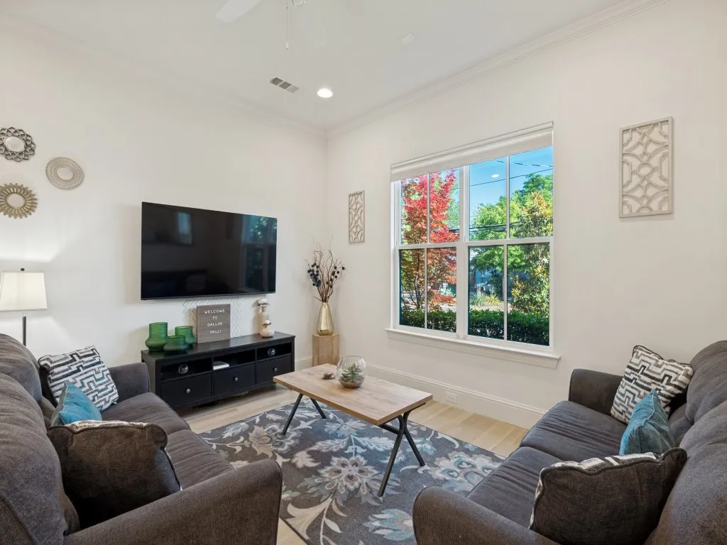 Living area featuring light wood-finish flooring, crisp white walls, and a large window with white trim