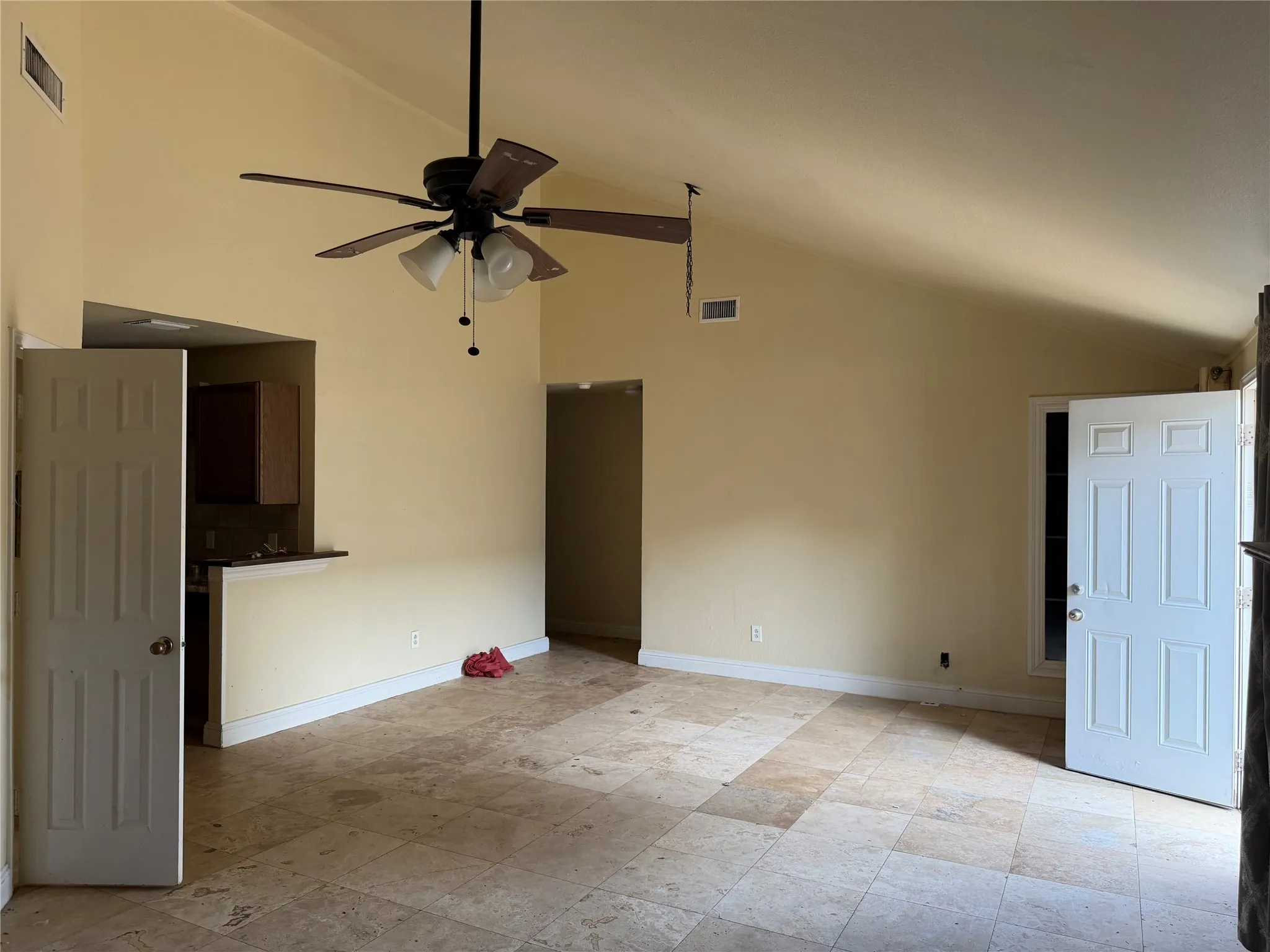 Spacious room featuring a vaulted ceiling with a ceiling fan, light-toned tile flooring, and a breakfast bar with wood cabinetry