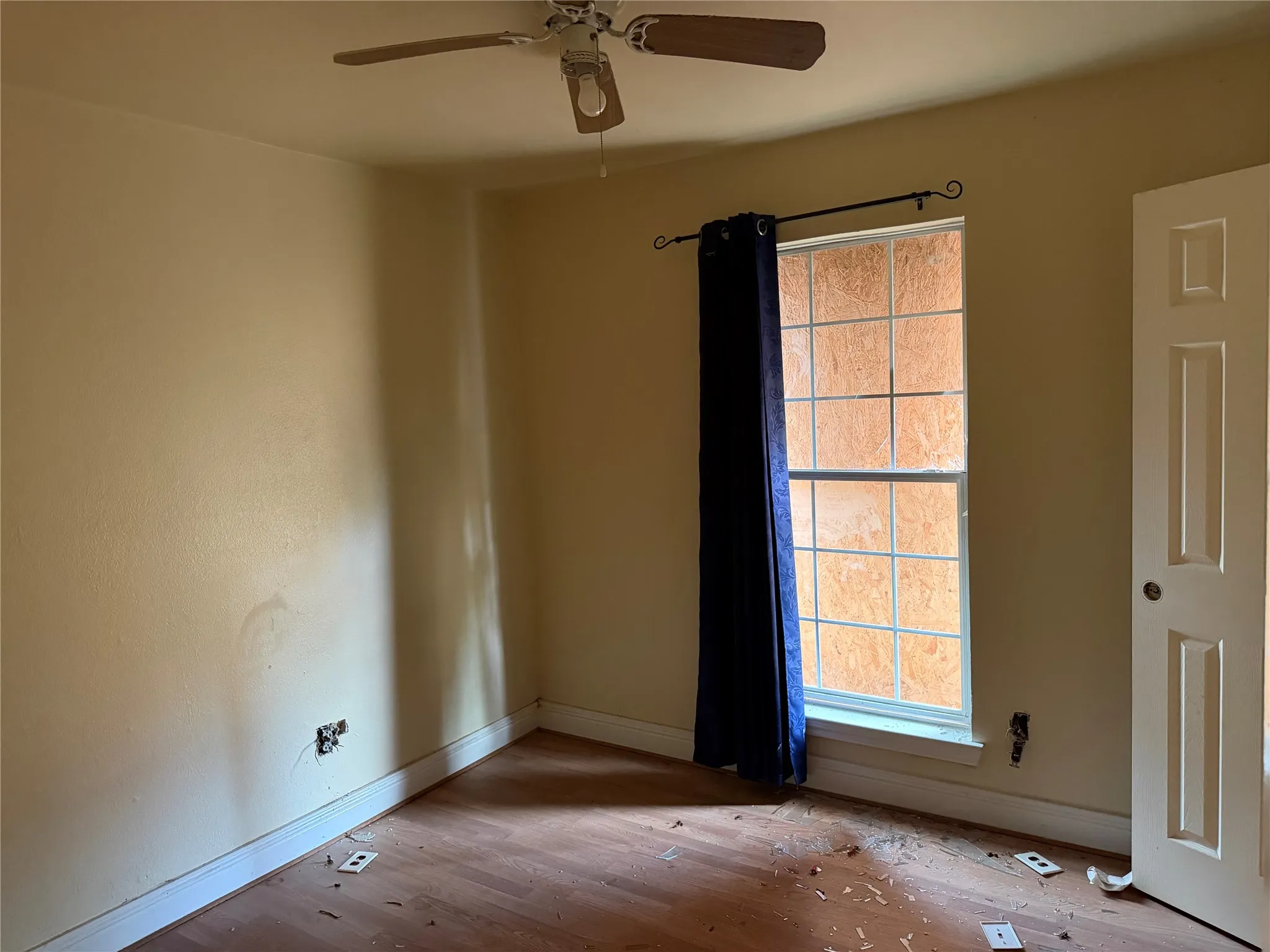 Wood-finish flooring, ceiling fan, single-panel door, and window with interior grid