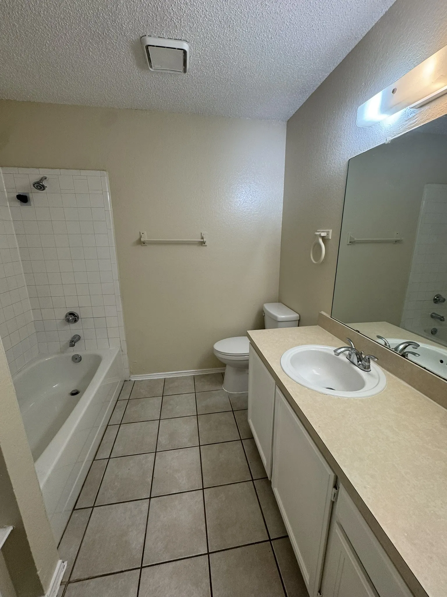White tiled flooring, vanity with integrated sink, toilet, and bathtub with tiled surround