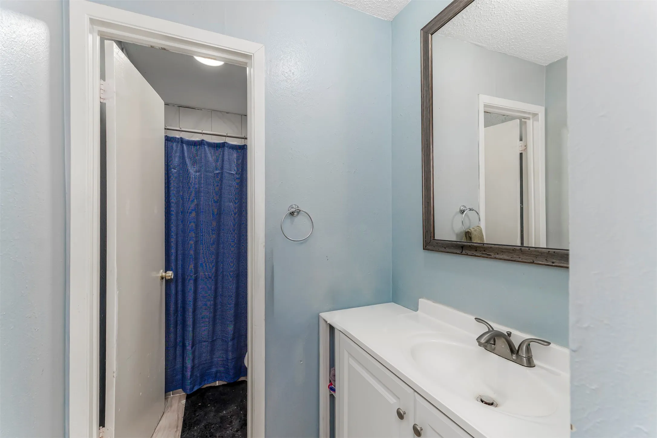 Vanity with an integrated sink and brushed nickel faucet, a large framed mirror, and a towel ring