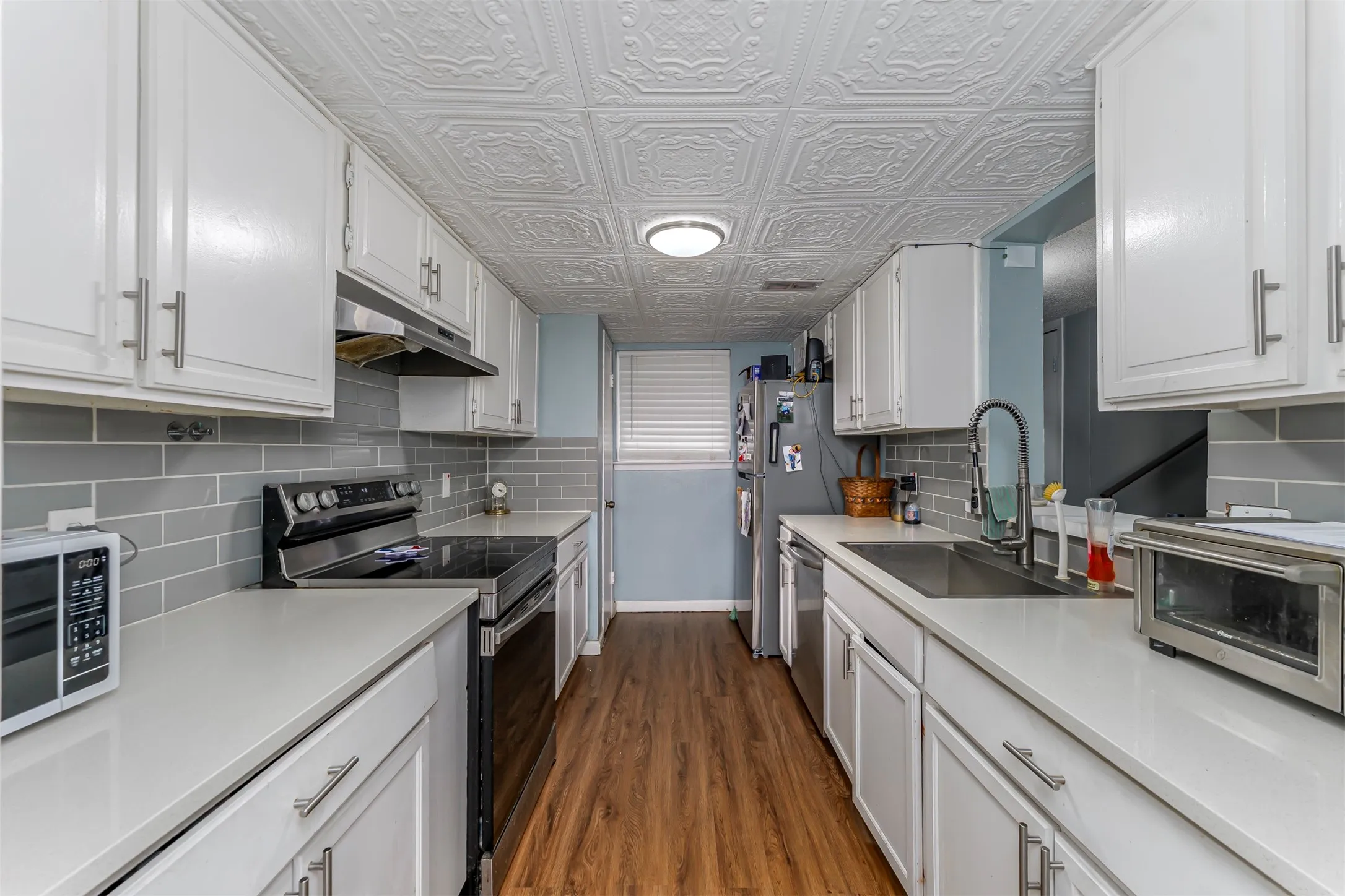 Galley kitchen featuring white cabinetry, light countertops, gray subway tile backsplash, and wood-finish flooring