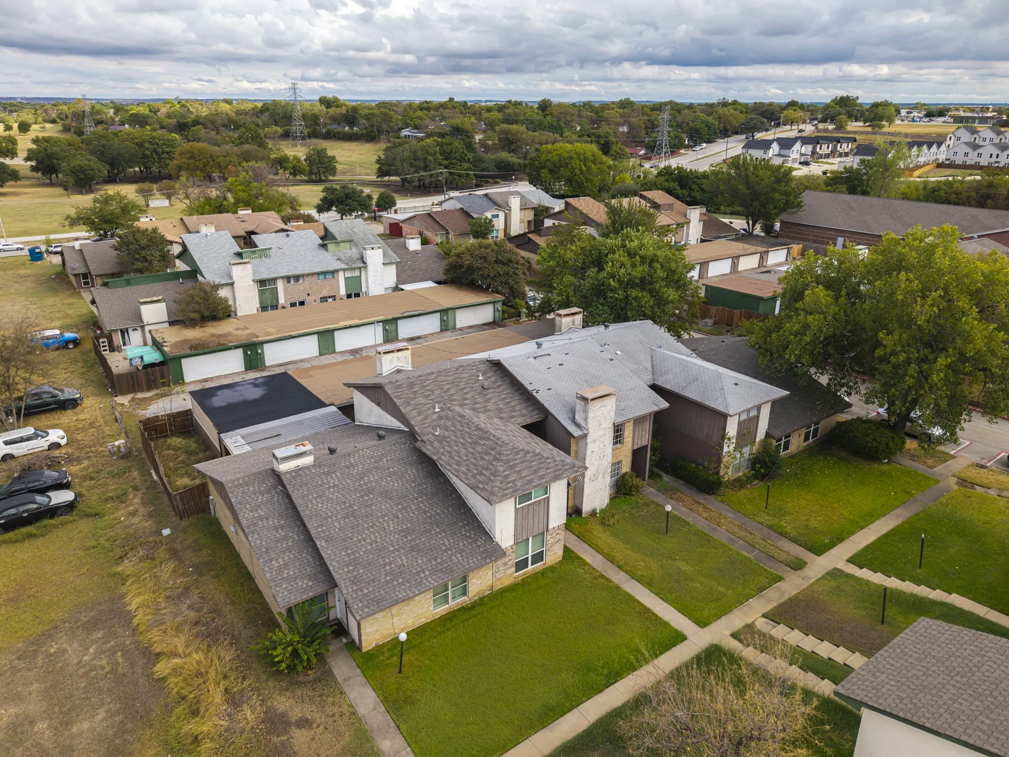 Multiple residential buildings with pitched shingle roofs, individual entryways, and adjacent green spaces