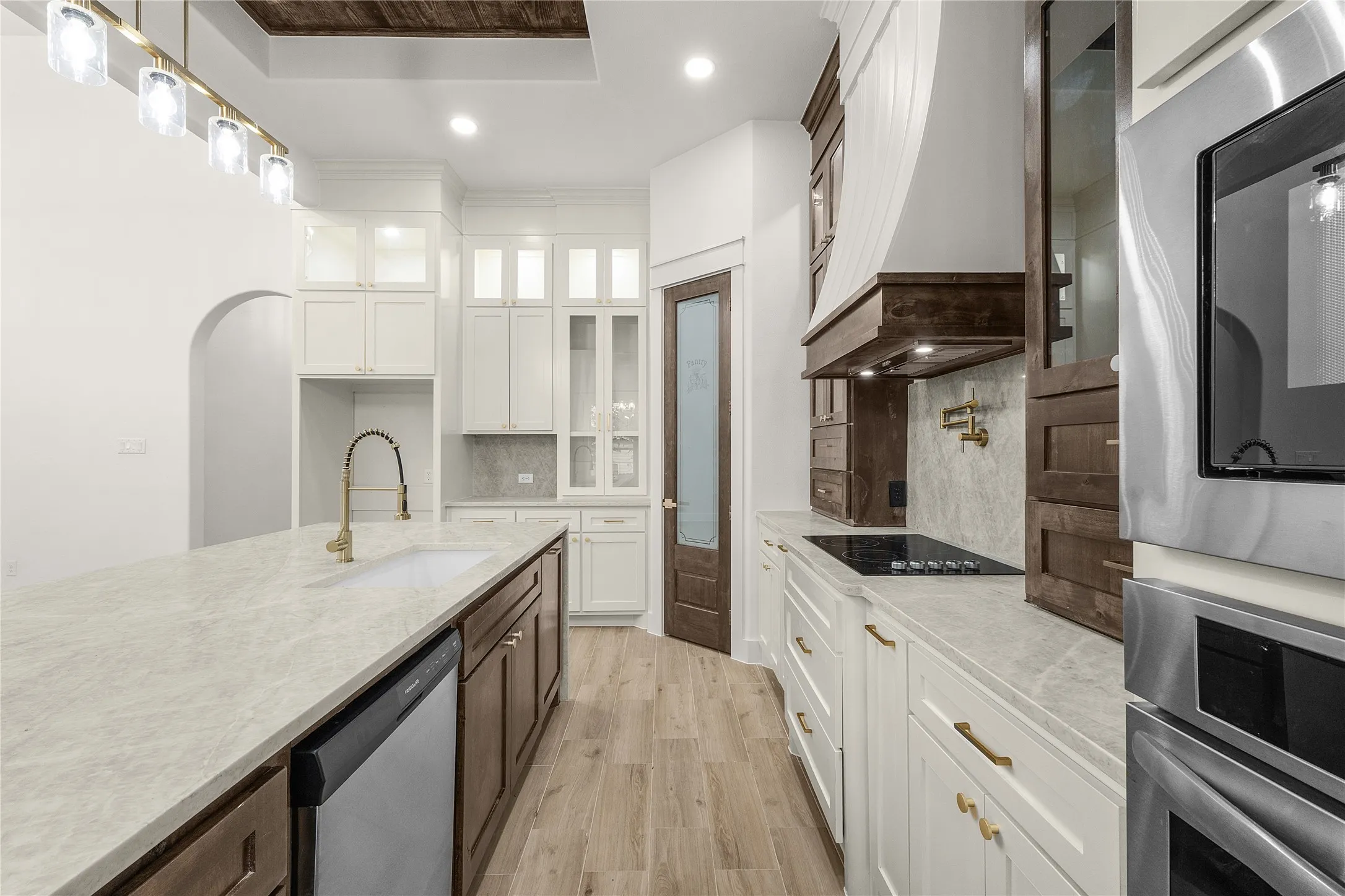 Gourmet kitchen with an expansive island, stone countertops, custom cabinetry, stainless steel appliances, and wood-finish flooring