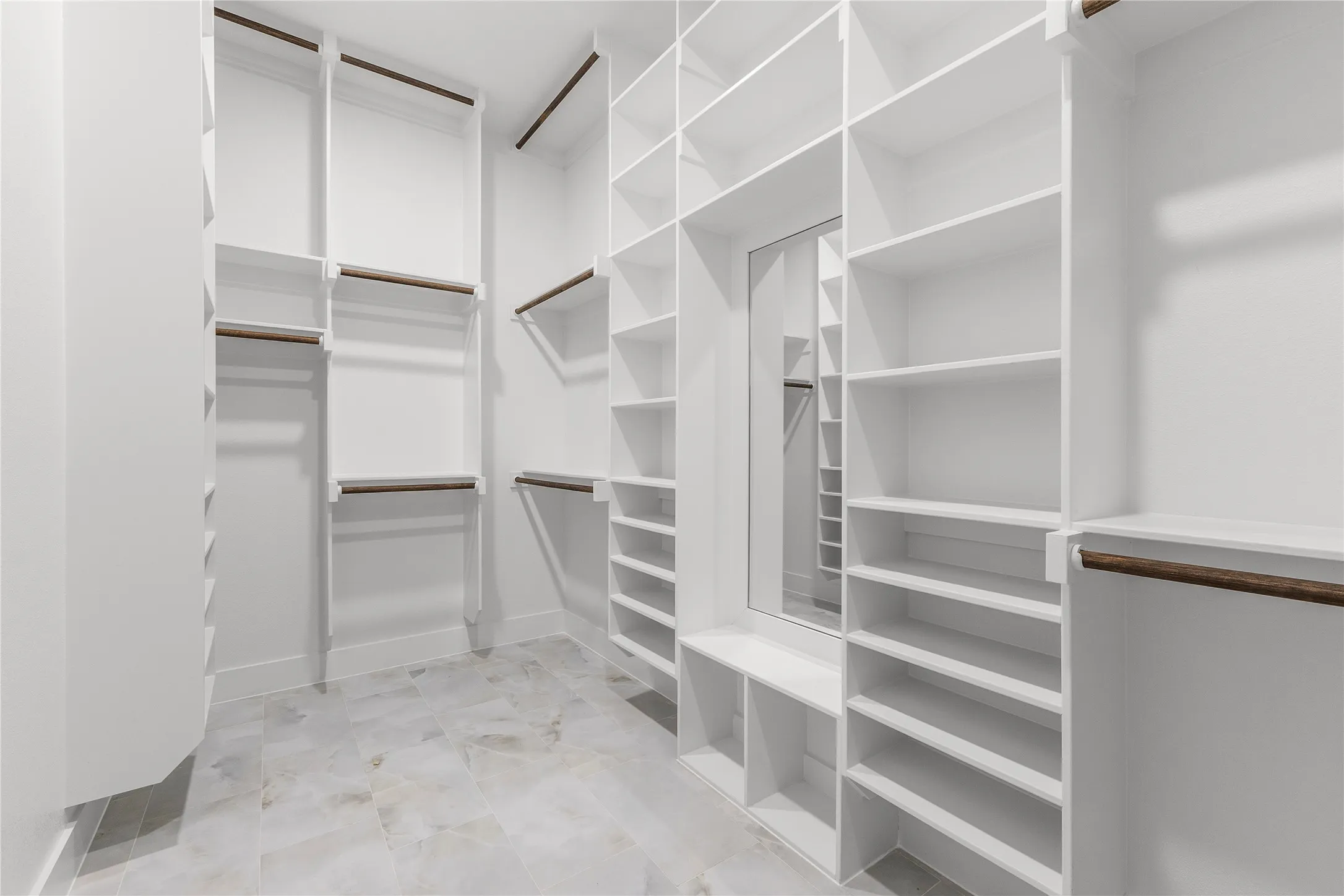 Walk-in closet with extensive built-in shelving, multiple hanging rods, a central built-in mirror, and light-toned tile flooring