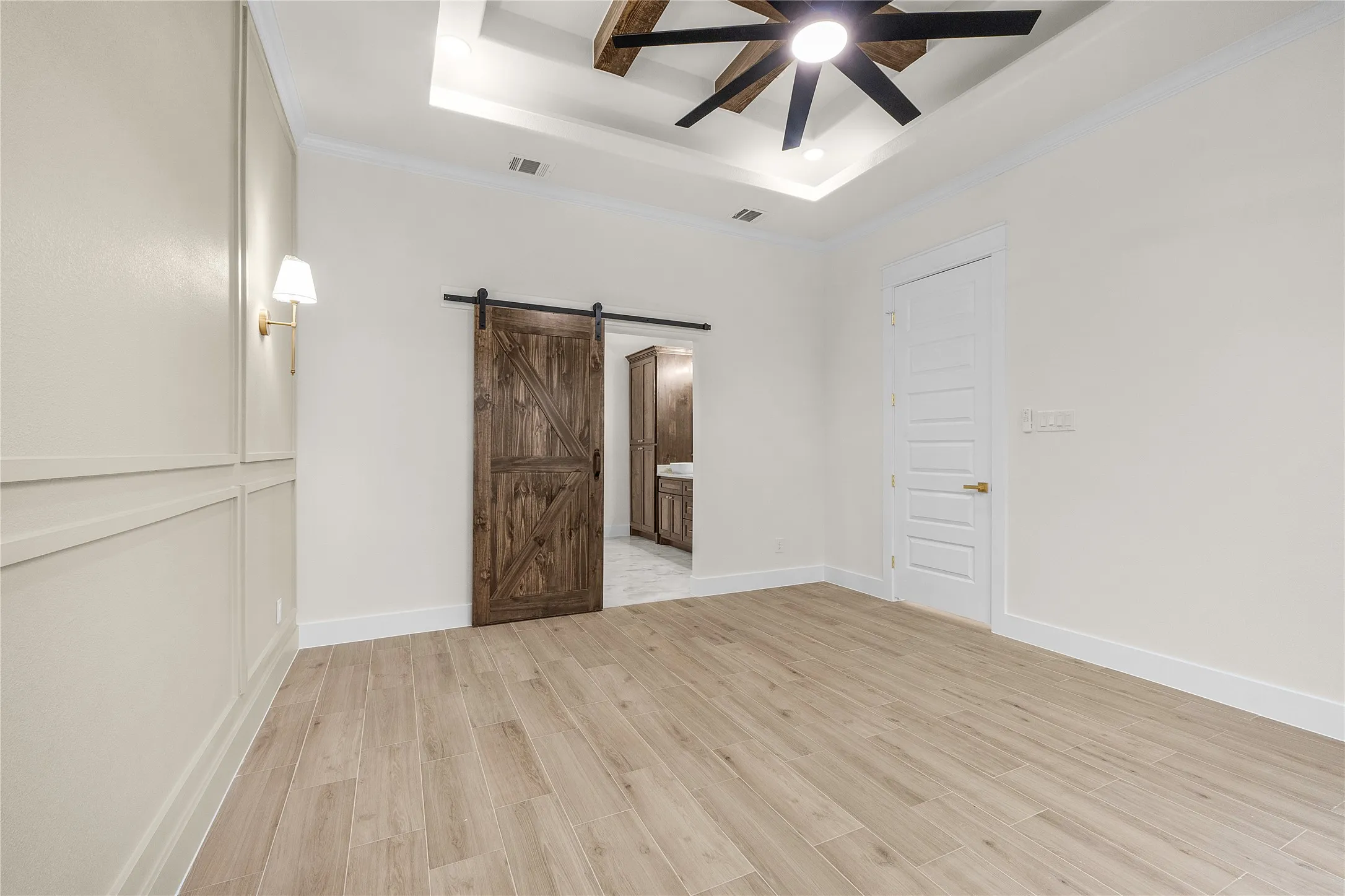 Wood-finish flooring, accent wall with panel molding, ceiling fan with wood-look blades, and a barn door