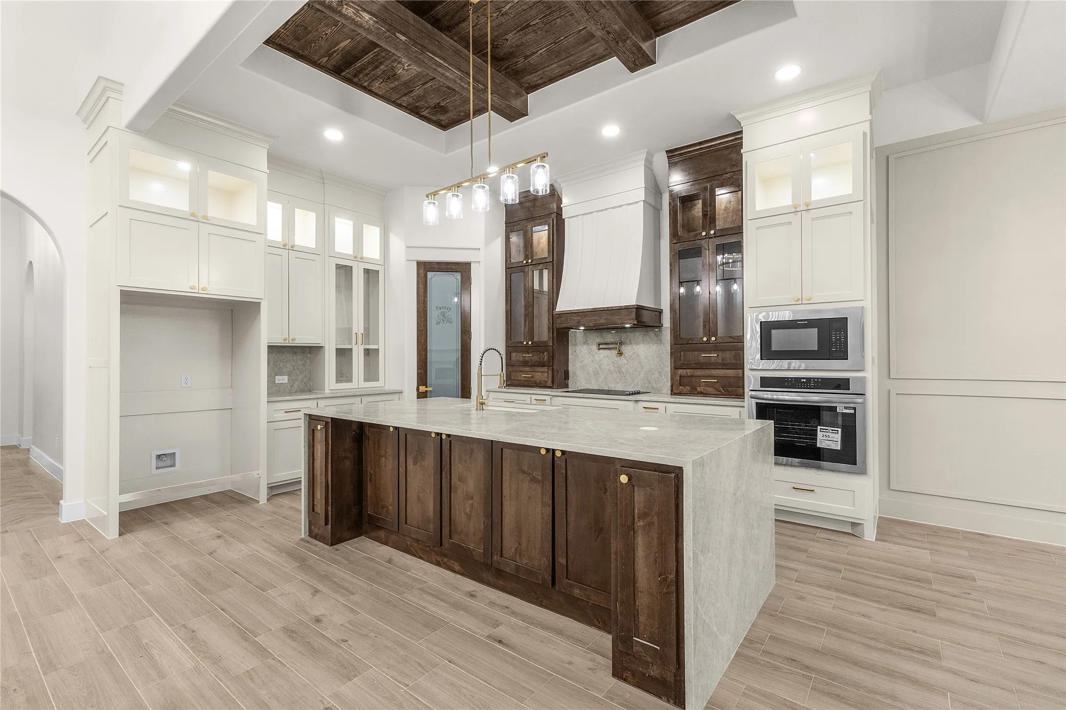 Kitchen featuring a central island with countertop, wood-finish flooring, custom cabinetry, and a coffered ceiling with exposed wood beams