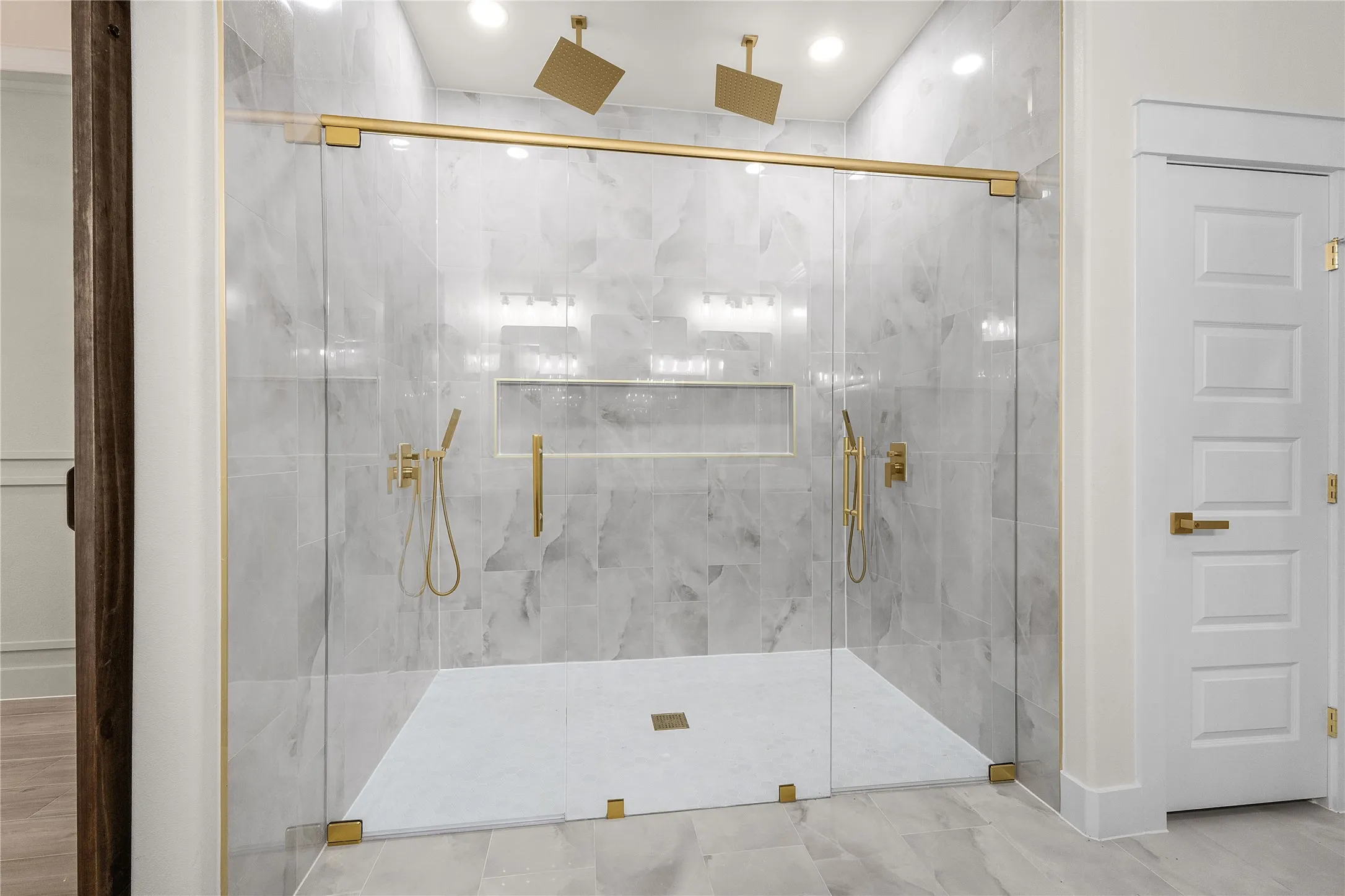 Spacious walk-in shower with floor-to-ceiling tile, dual rain shower heads, a built-in niche, and gold-finish hardware