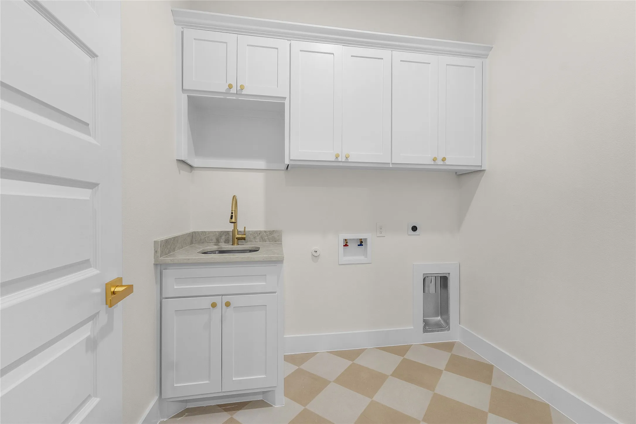 White shaker cabinetry with gold-tone hardware, granite countertop with undermount sink, gold-tone faucet, and checkered floor tile