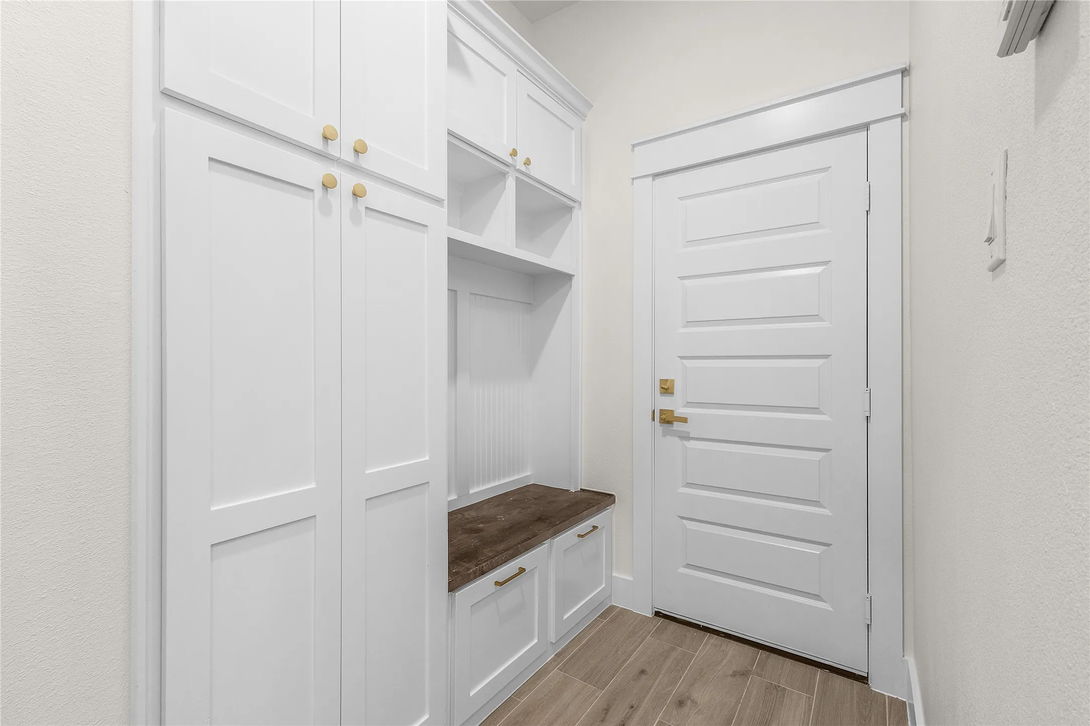 Built-in white cabinetry with gold-finish hardware, wood-finish bench, and wood-look flooring