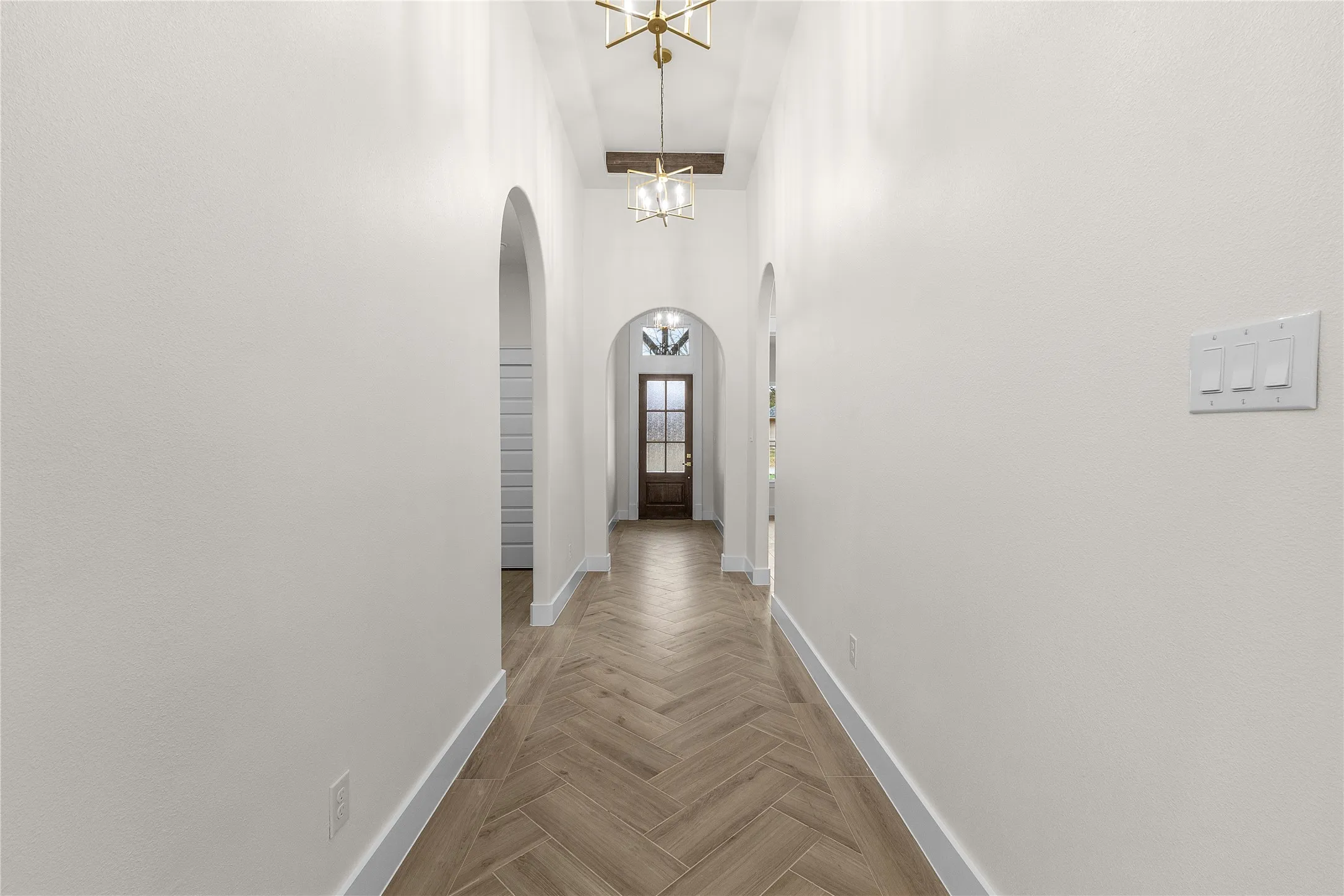 Herringbone wood-finish flooring, arched doorways, white walls, and built-in ceiling lighting