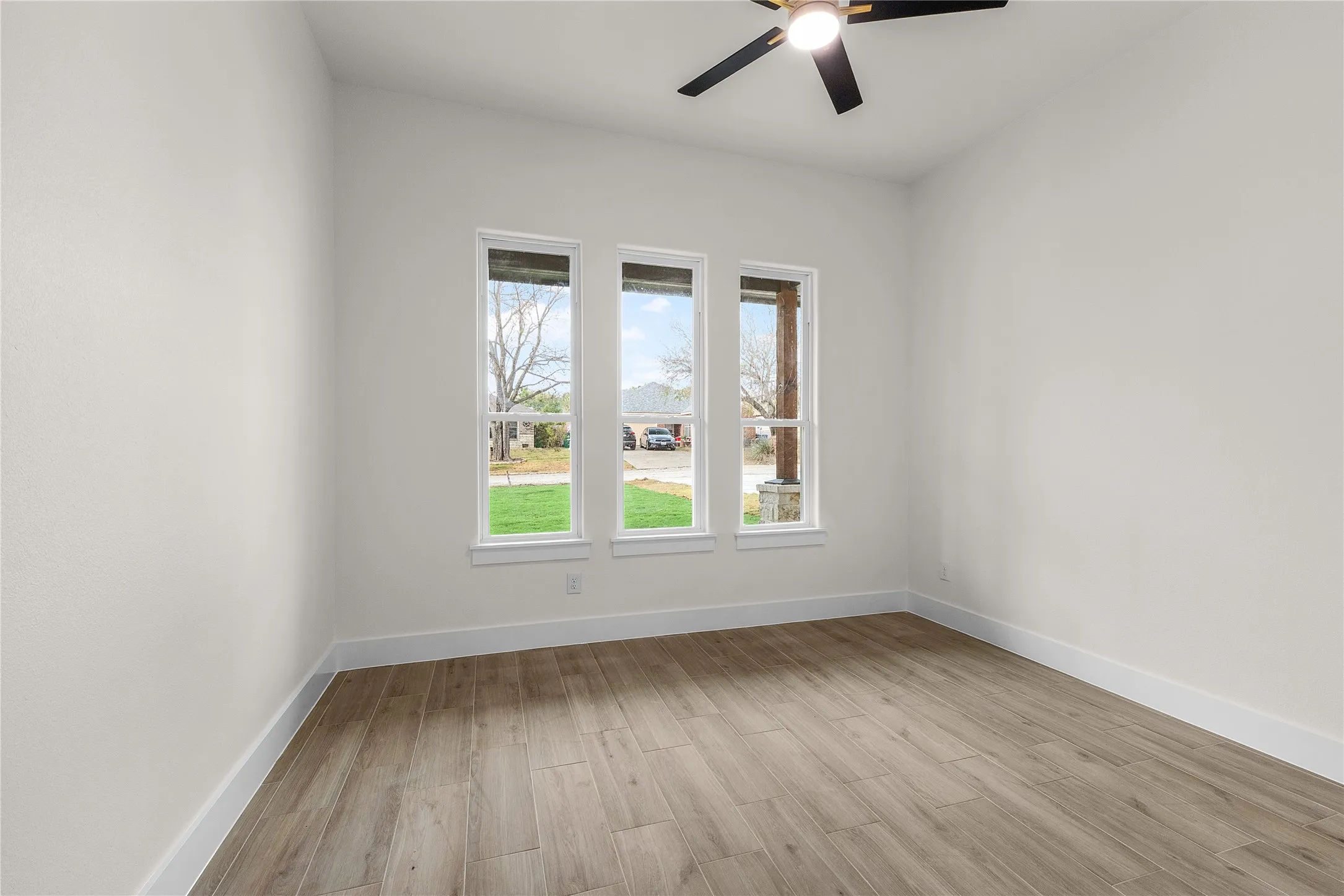 Wood-finish flooring, three large windows, white trim, and a ceiling fan with integrated lighting