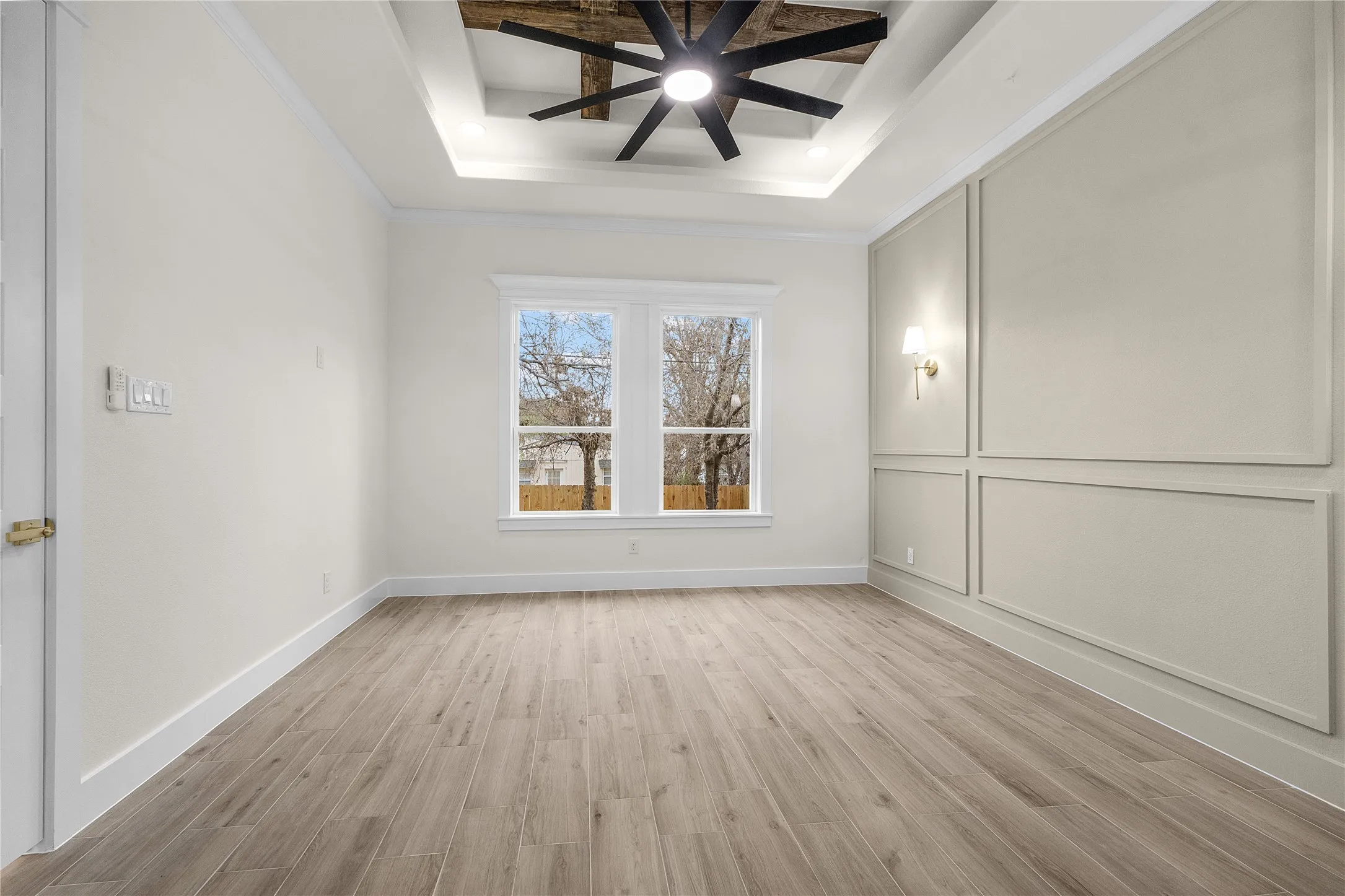 Tray ceiling with wood-finish inserts and a ceiling fan, wall paneling with sconce lighting, wood-finish flooring, and white trim