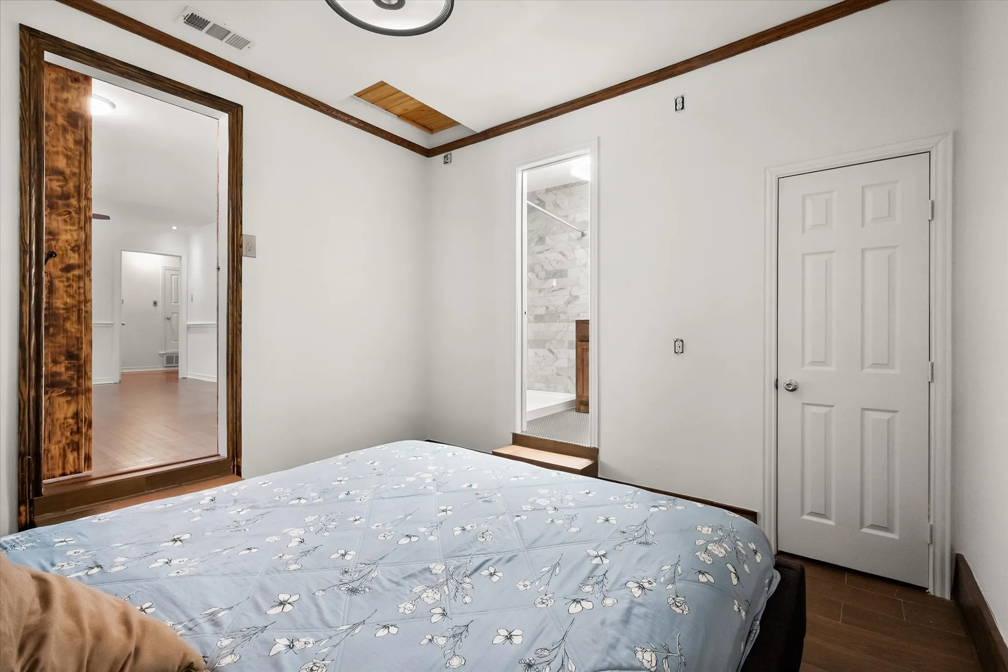 Wood-finish flooring with white baseboards, wood-trim ceiling details, and a six-panel door