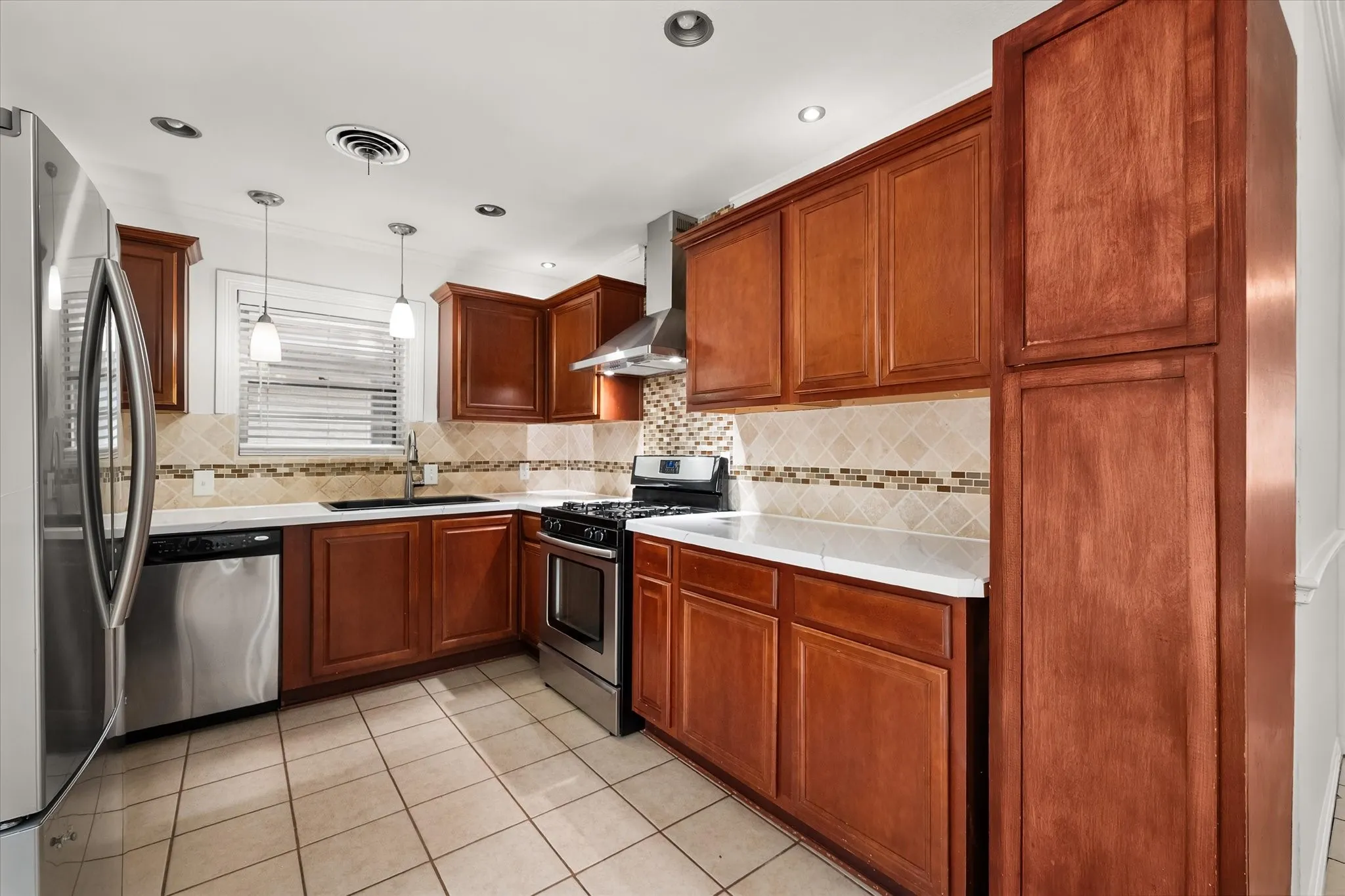 Kitchen featuring rich wood cabinetry, stainless steel appliances, light countertops, a decorative tile backsplash, and recessed lighting