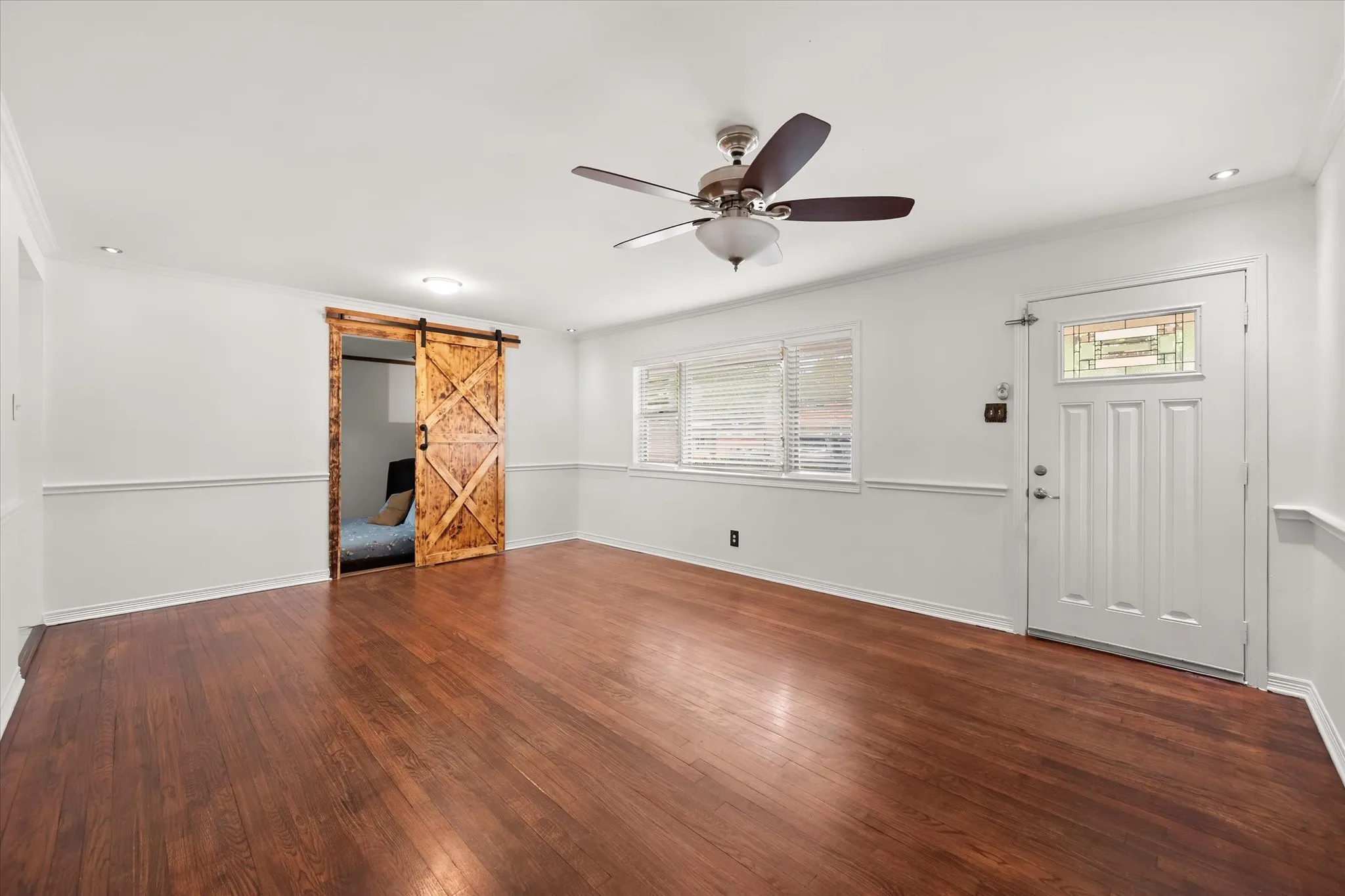 Wood-finish flooring, ceiling fan with integrated lighting, recessed lighting, barn door, and a front entry door with a stained glass insert