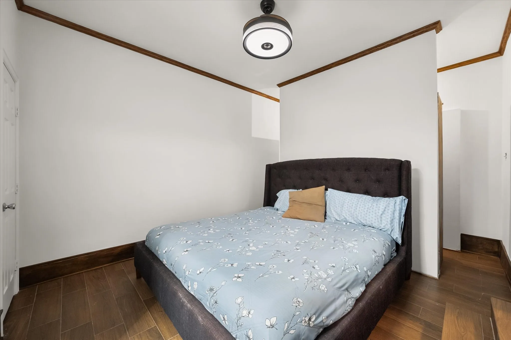 Wood-finish flooring with coordinating wood trim, crown molding, and a modern ceiling light fixture