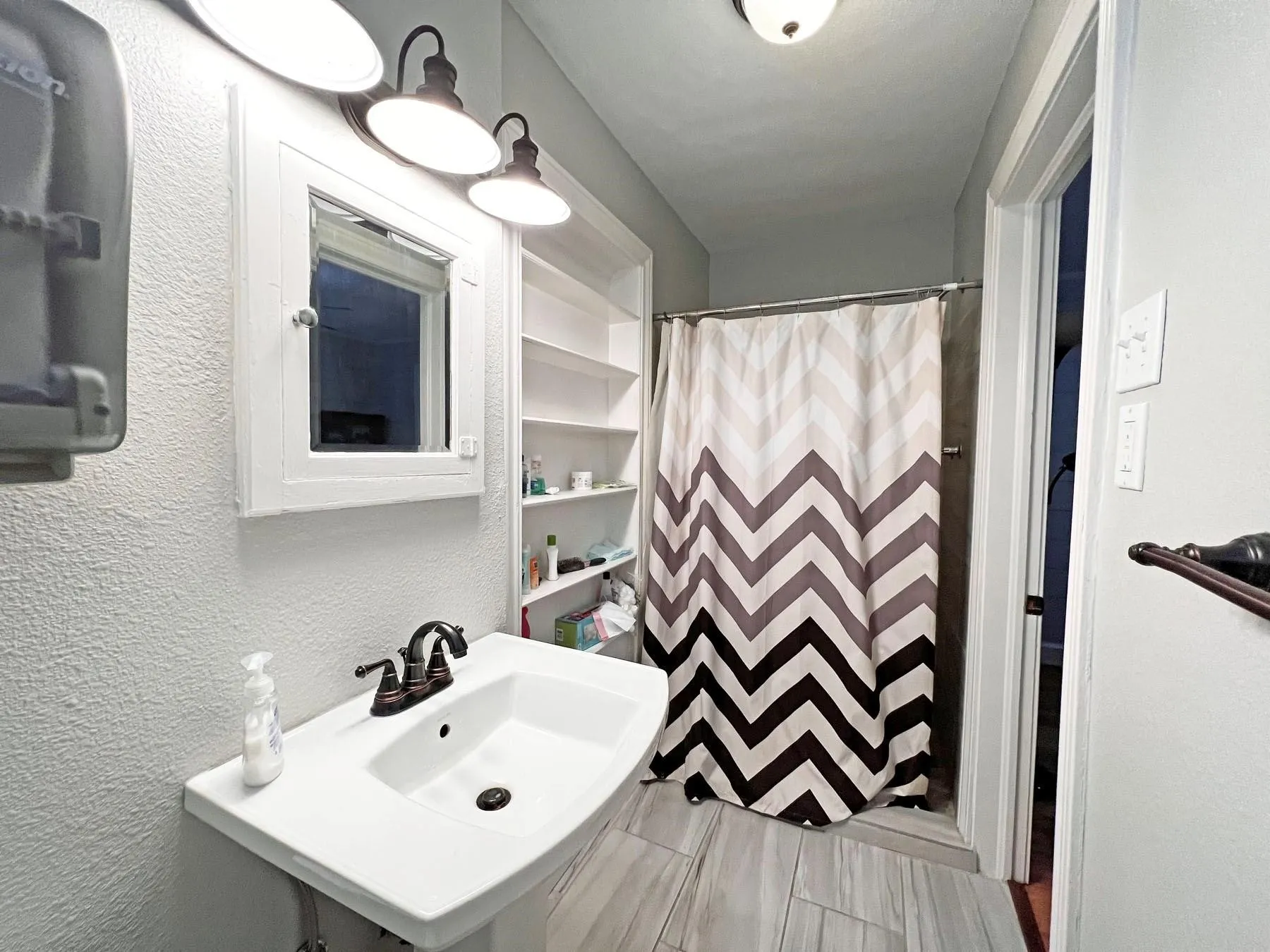 Pedestal sink with bronze-finish faucet, built-in shelving, white medicine cabinet, and overhead vanity lighting
