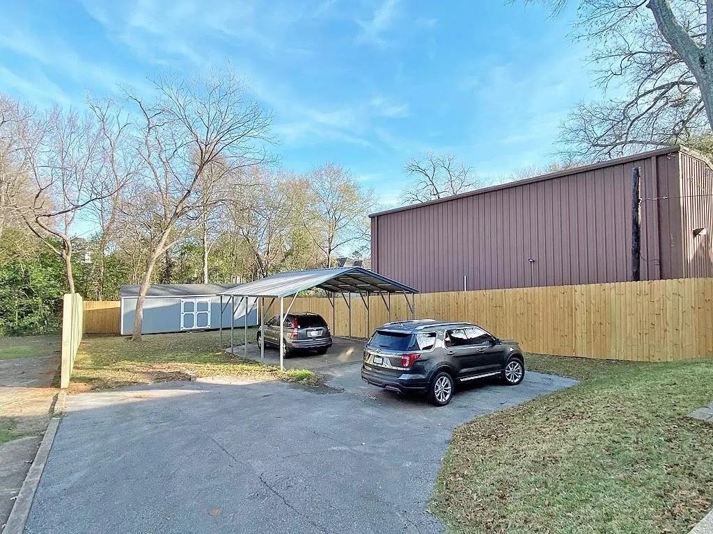 Paved parking area, metal carport, wood privacy fence, detached storage shed, and mature trees