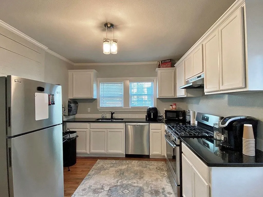 Kitchen featuring wood-finish flooring, white cabinetry, black countertops, and stainless steel appliances