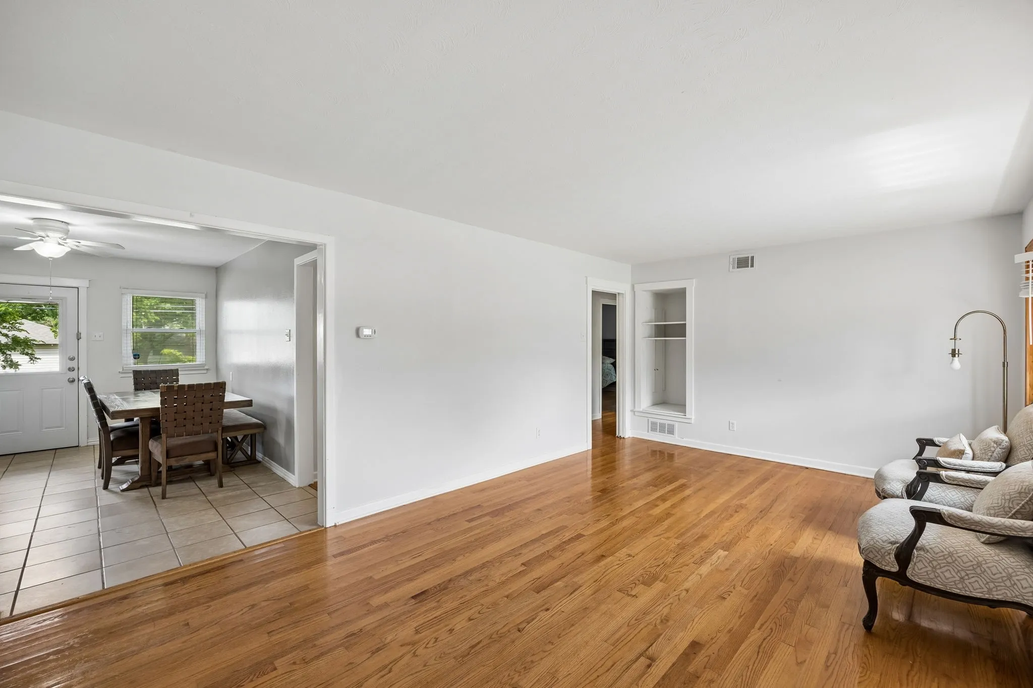 Hardwood flooring in living area, built-in shelving, tiled flooring in dining area, ceiling fan, and white trim throughout
