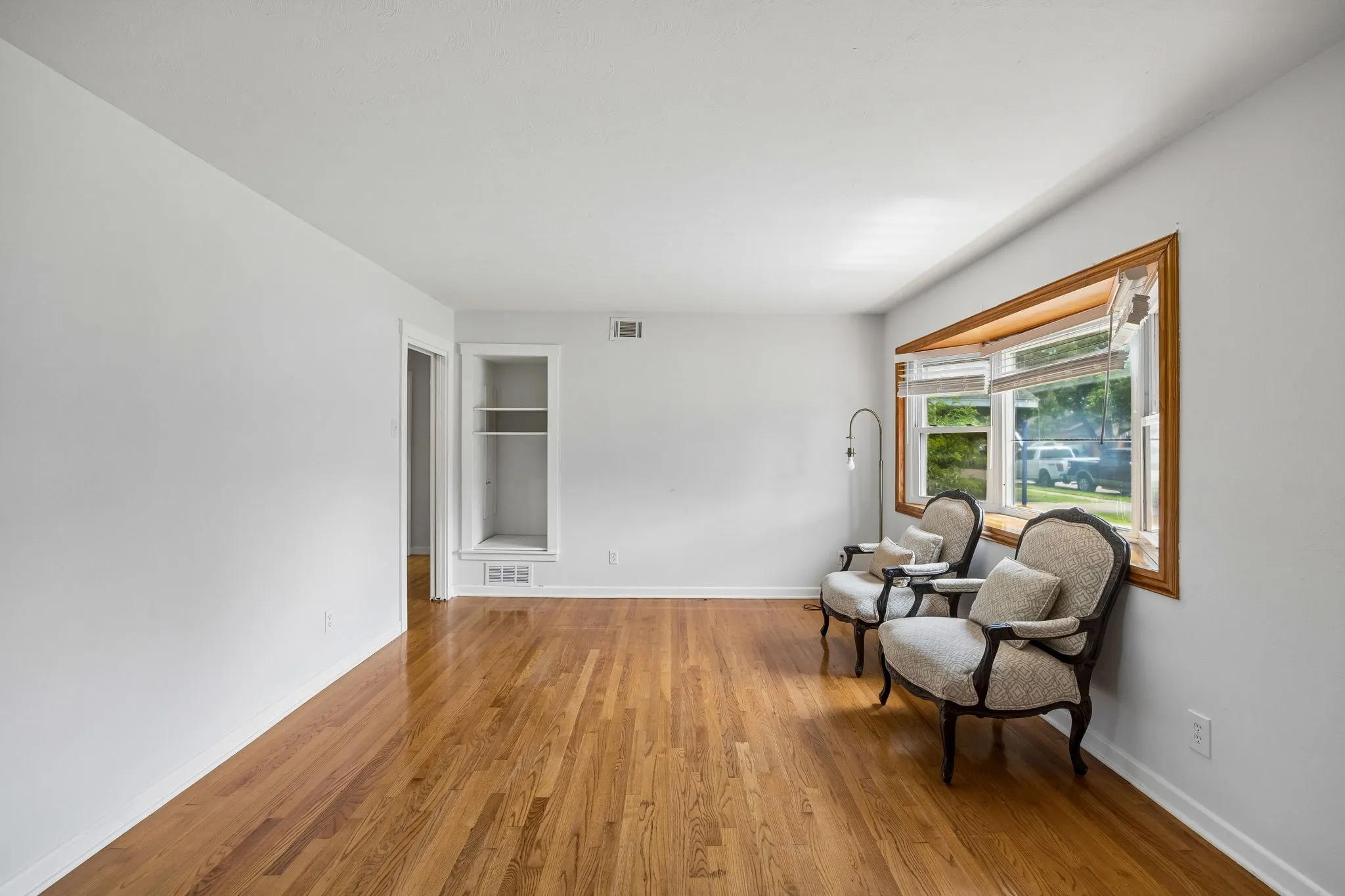Wood-finish flooring, recessed built-in shelving, and a bay window with wood trim
