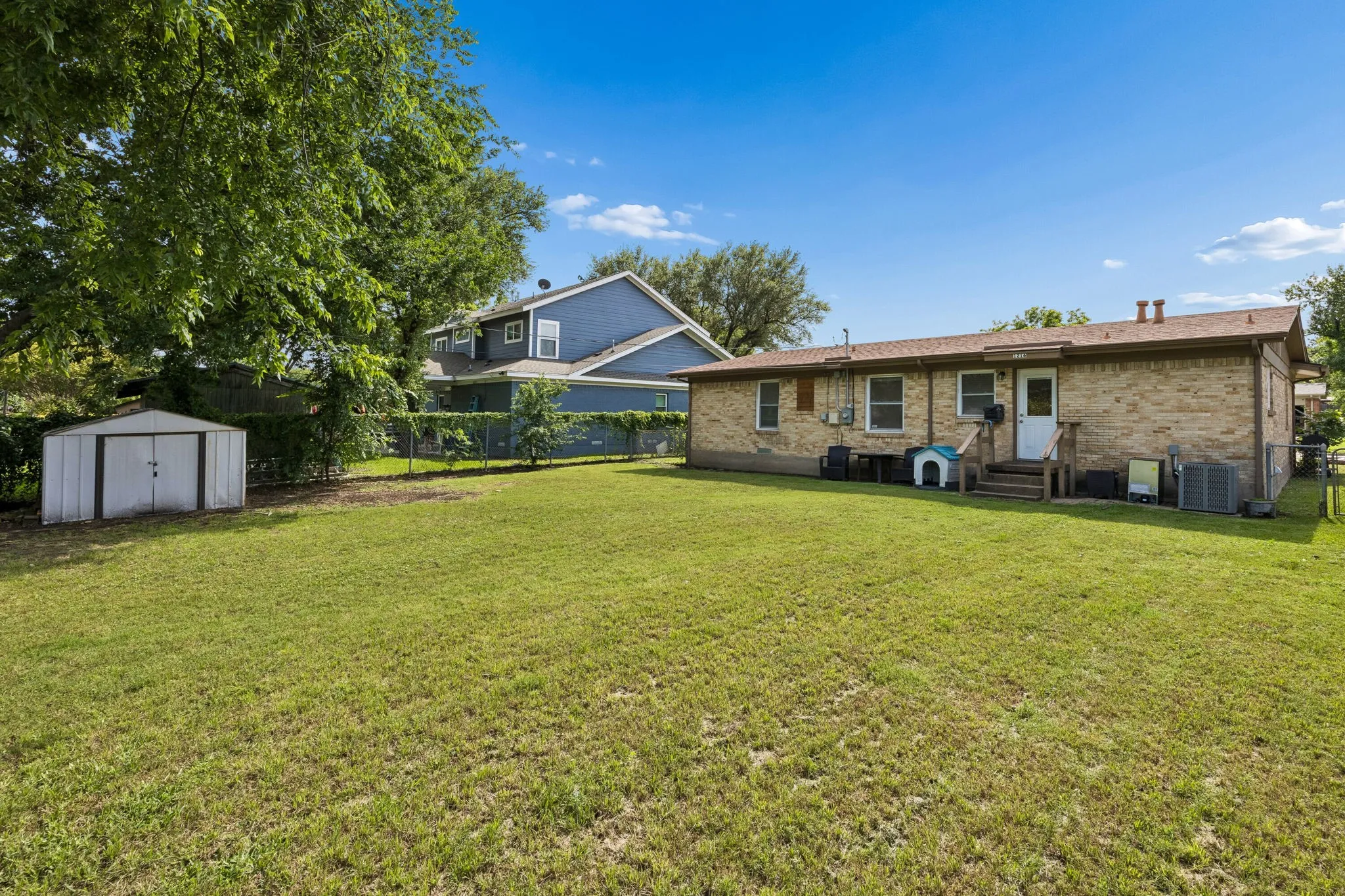 Expansive backyard featuring a manicured lawn, a detached storage shed, a brick exterior, and a rear entrance with stairs