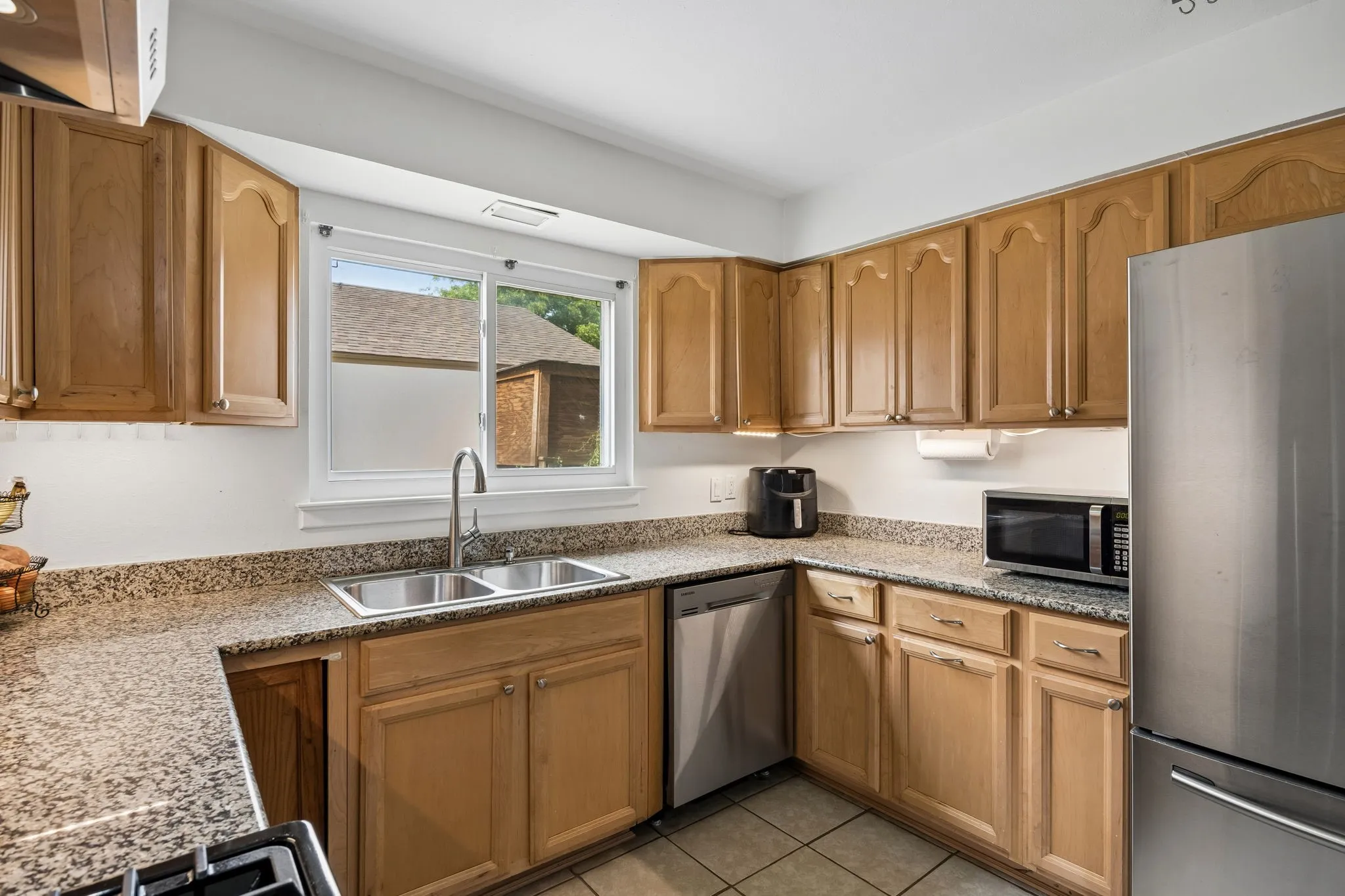 Kitchen featuring wood-finish cabinetry, speckled countertops, a stainless steel double basin sink, and tile flooring